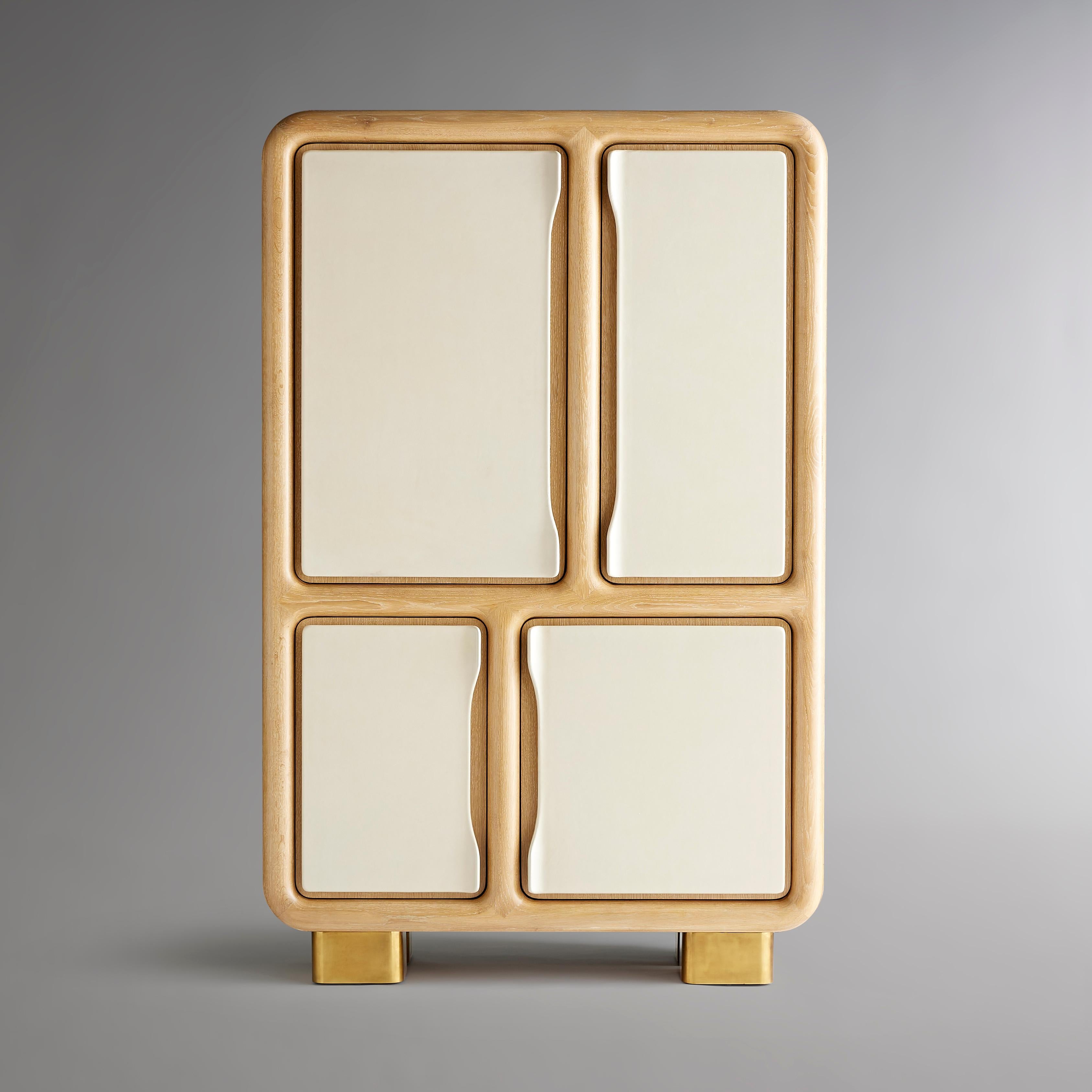 Elegant curvature accents this cabinet from sculpted pulls that flair out from the doors, to the masterful framework, to rounded feet of burnished brass. The doors are covered in ivory leather, which brings out the cerused wood highlights of
