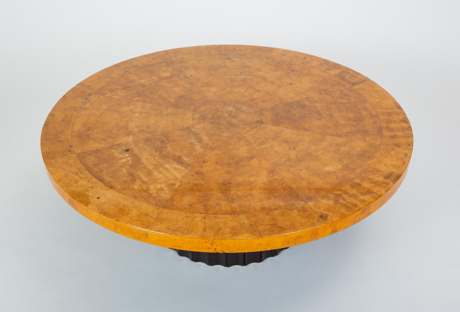 A 1970s round coffee table with a plinth base and distinguished lacquered surface. The custom-built piece has a circular wooden frame wrapped in parchment and finished with a high-gloss lacquer coat. Individual pieces of the parchment have been