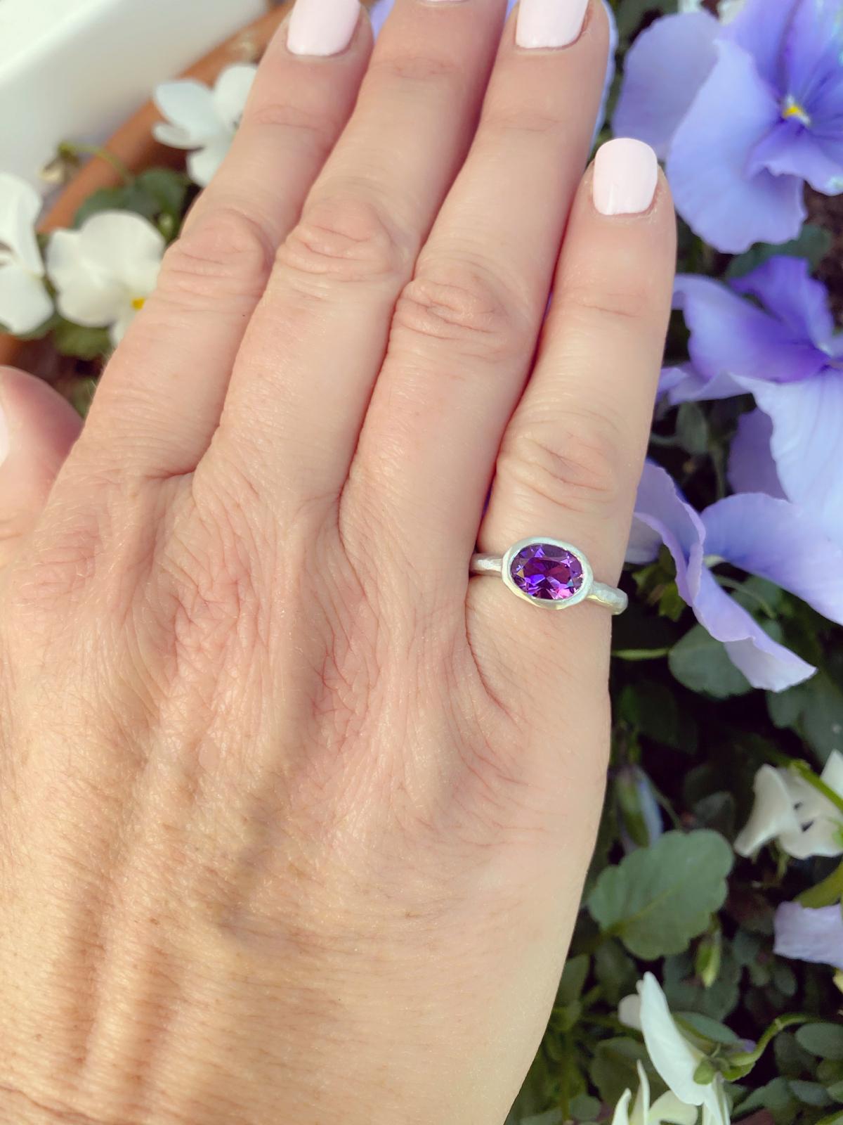 Handmade and custom, this one-of-a-kind ring features an oval-shaped bright purple amethyst weighing 1.04 carats, horizontally bezel-set in a textured, hammered 18k white gold contemporary mount. Showcasing exceptional light return and even color