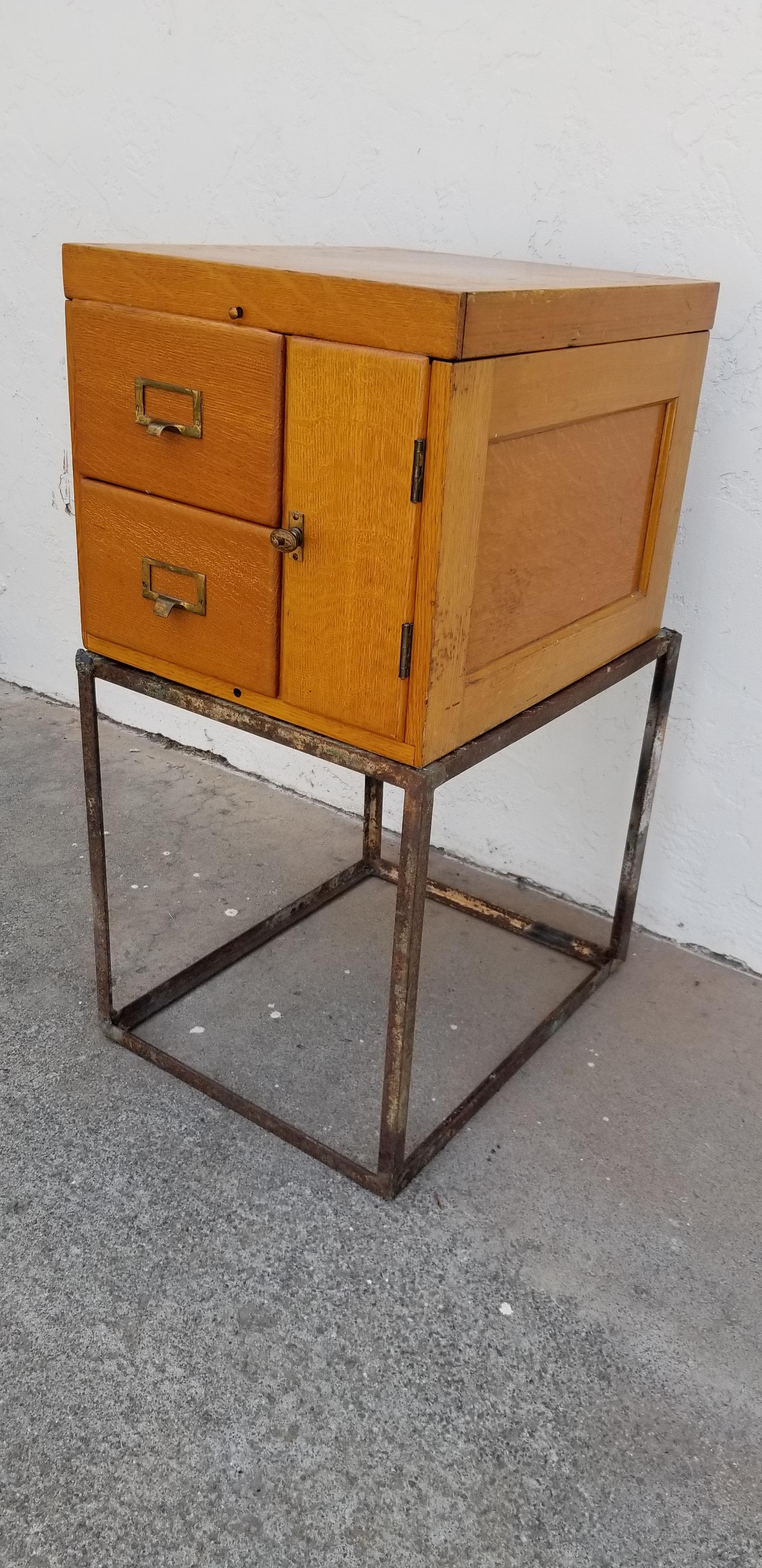 Nice marriage of an early 1900s oak file cabinet to an Industrial angle iron base. Good patina to iron base. Cabinet consists of two files and storage area. Original hardware and finish to cabinet. Could work as an end table or entry piece. Unique.