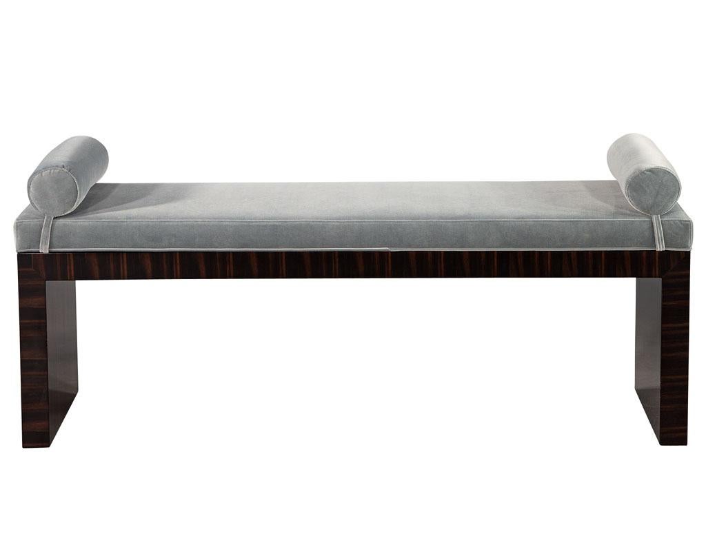 This bench is part of the Carrocel custom collection. Hand crafted and hand polished in Macassar wood. It is upholstered in a classic pale grayish blue velvet with attached bolsters on the ends for added detail. This bench is a timeless, yet modern