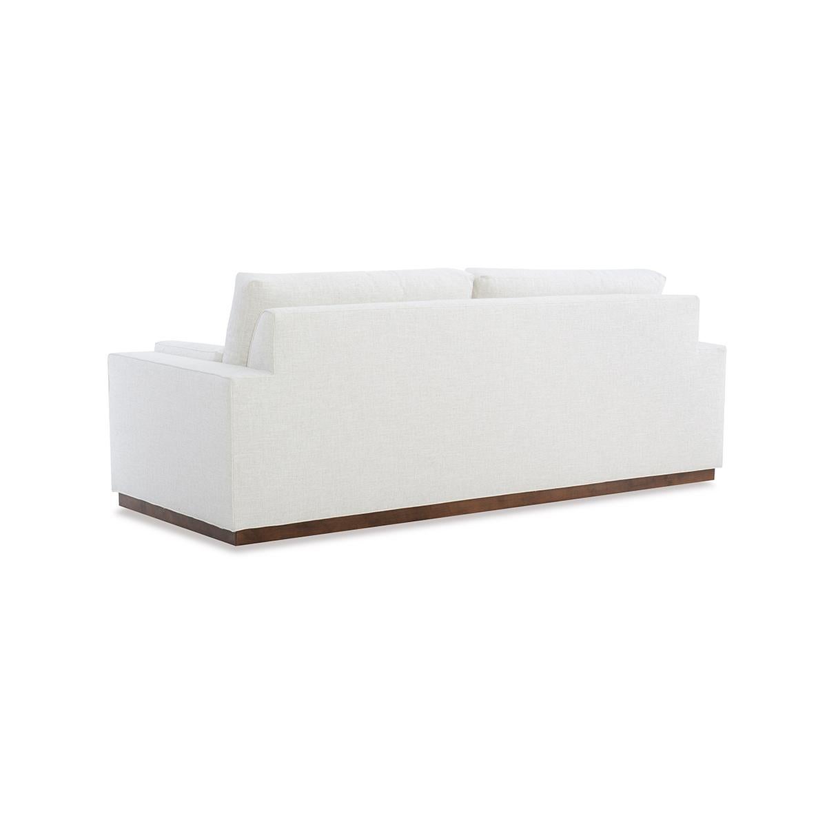 With two loose back cushions and a boxed cushion seat, with low profile arms, raised on a simple stepped-back wooden plinth base.

Proudly made in the USA, each piece boasts traditional 8-way hand-tied construction and toxin-free, kiln-dried solid