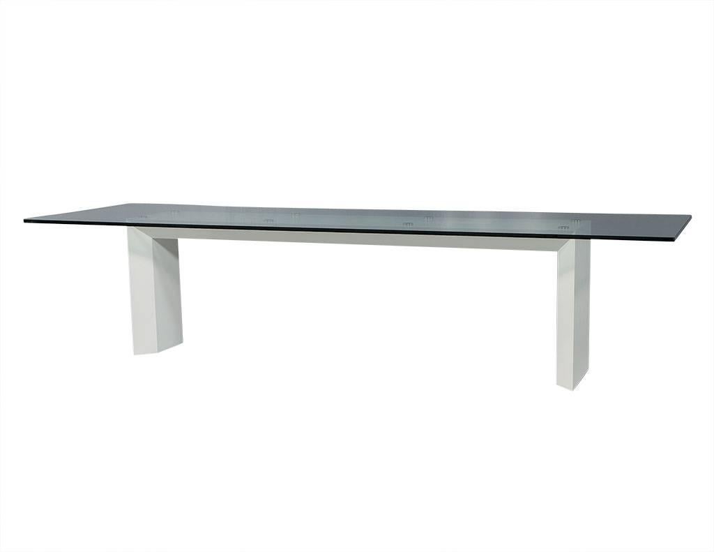 This modern dining table is made to order. It is crafted out of thick glass sitting atop a lacquered, sculpted and beveled base with hidden reinforced steel. Underneath the glass are eight round, polished, steel support pieces that keep the tabletop