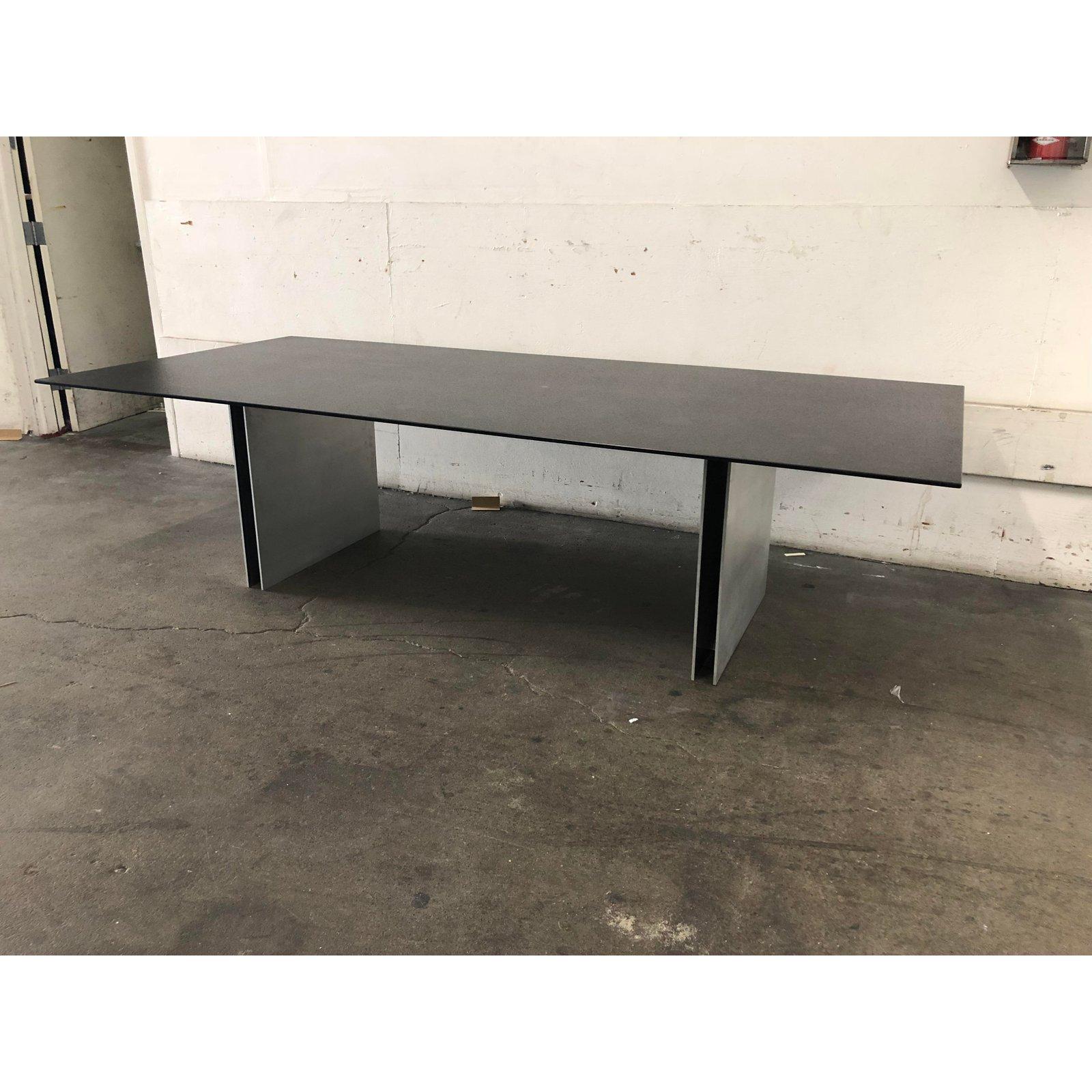 A modern and Industrial style dining table. A textured black top rests on double reinforced twin steel pedestals. The combination of faux stone and industrial steel materials combined with simple geometry and razor sharp lines make this piece a