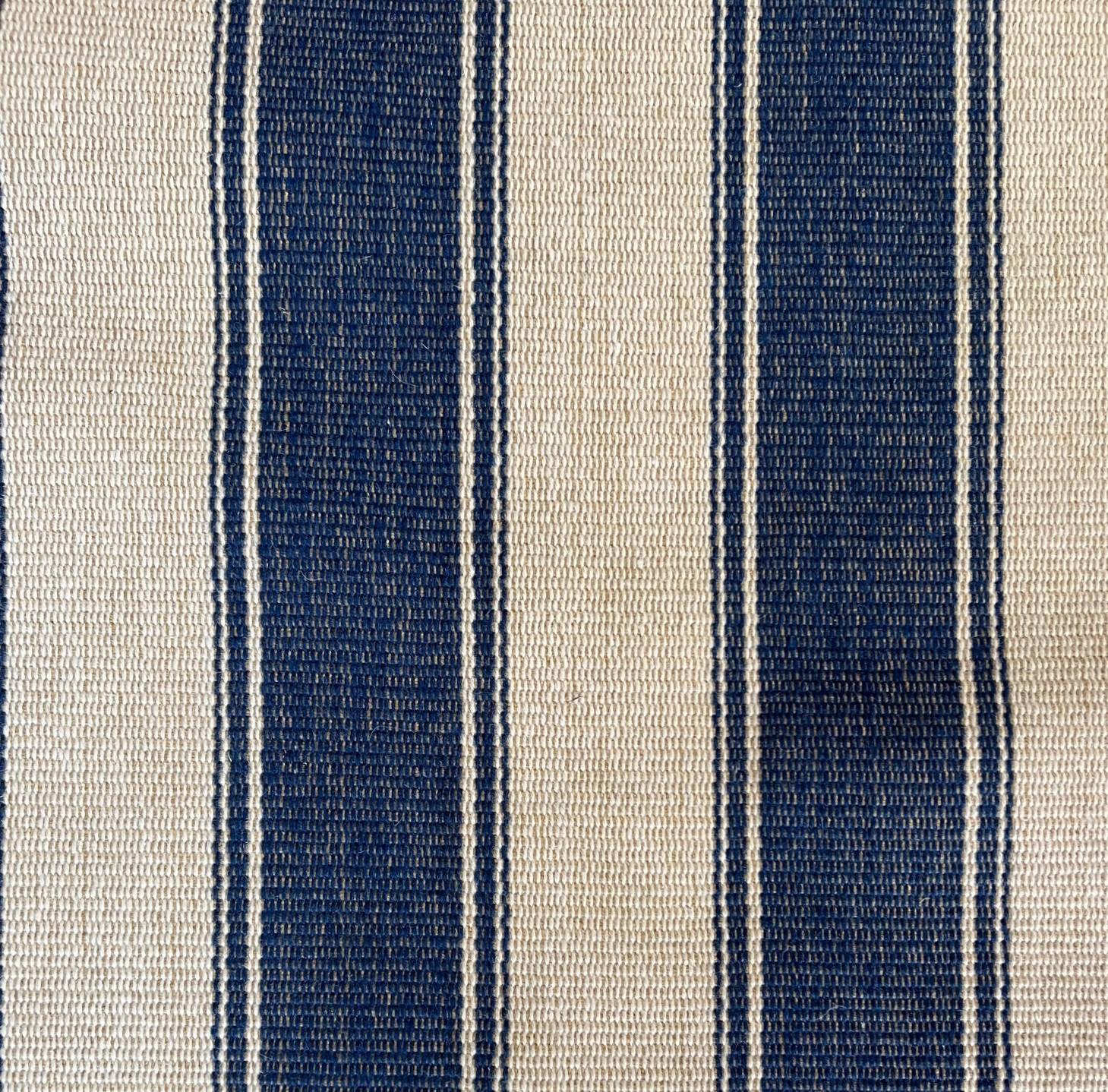 A striking modern custom striped area rug with faux leather edging and brass accents. This blue and light beige floor covering certainly makes a statement. The unexpected yet effective use of the edging studded with oversized brass nailhead trim