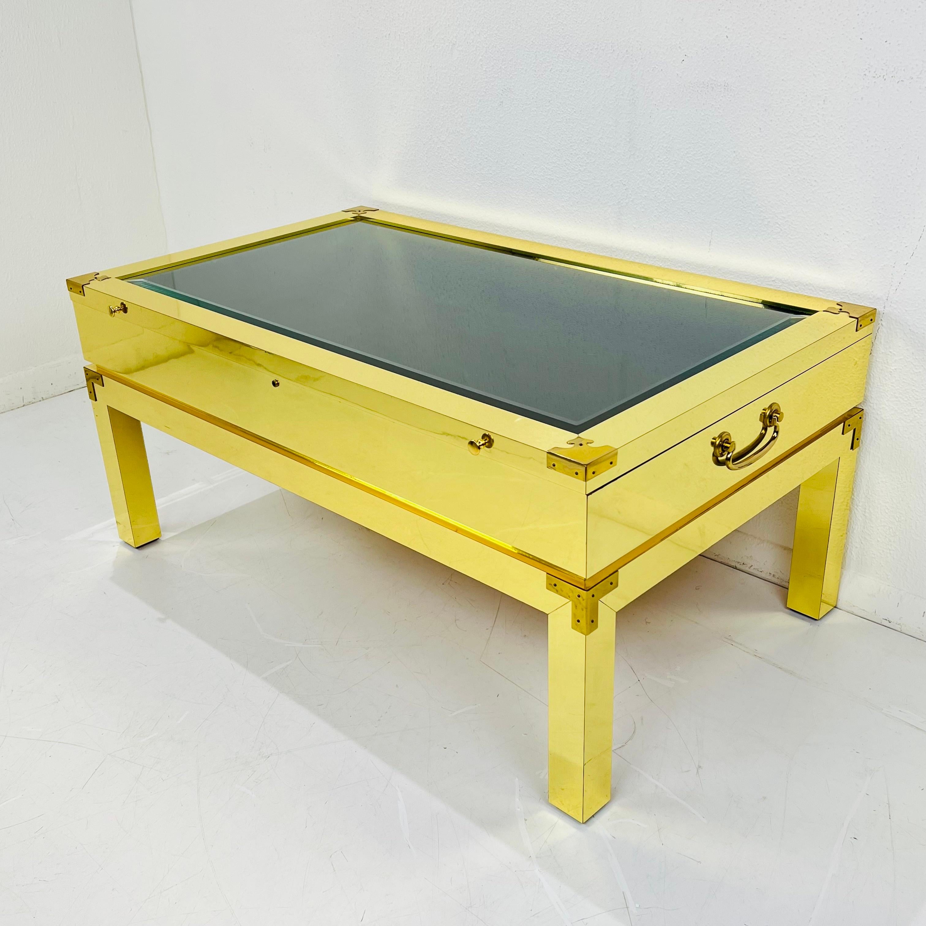 Unique brass wrapped campaign style display coffee table. Thick glass top opens to a soft lined interior, and the full piece is wrapped in brass and supported by square block legs. One of a kind! Very good, lightly used condition. 