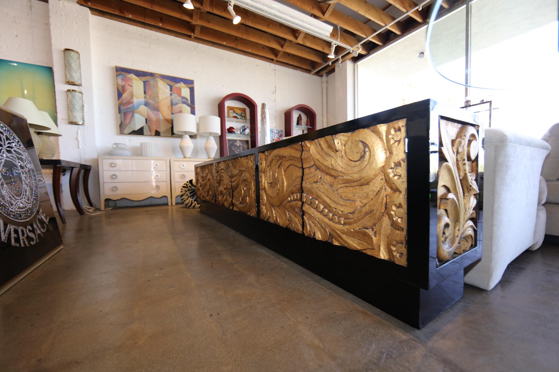 A custom made 10 foot long credenza with six doors and two carved wood end panels that are gold leafed. The piece has four compartments with a glass shelf. The piece has been re-lacquered and clear coated. The panels have been left alone. The