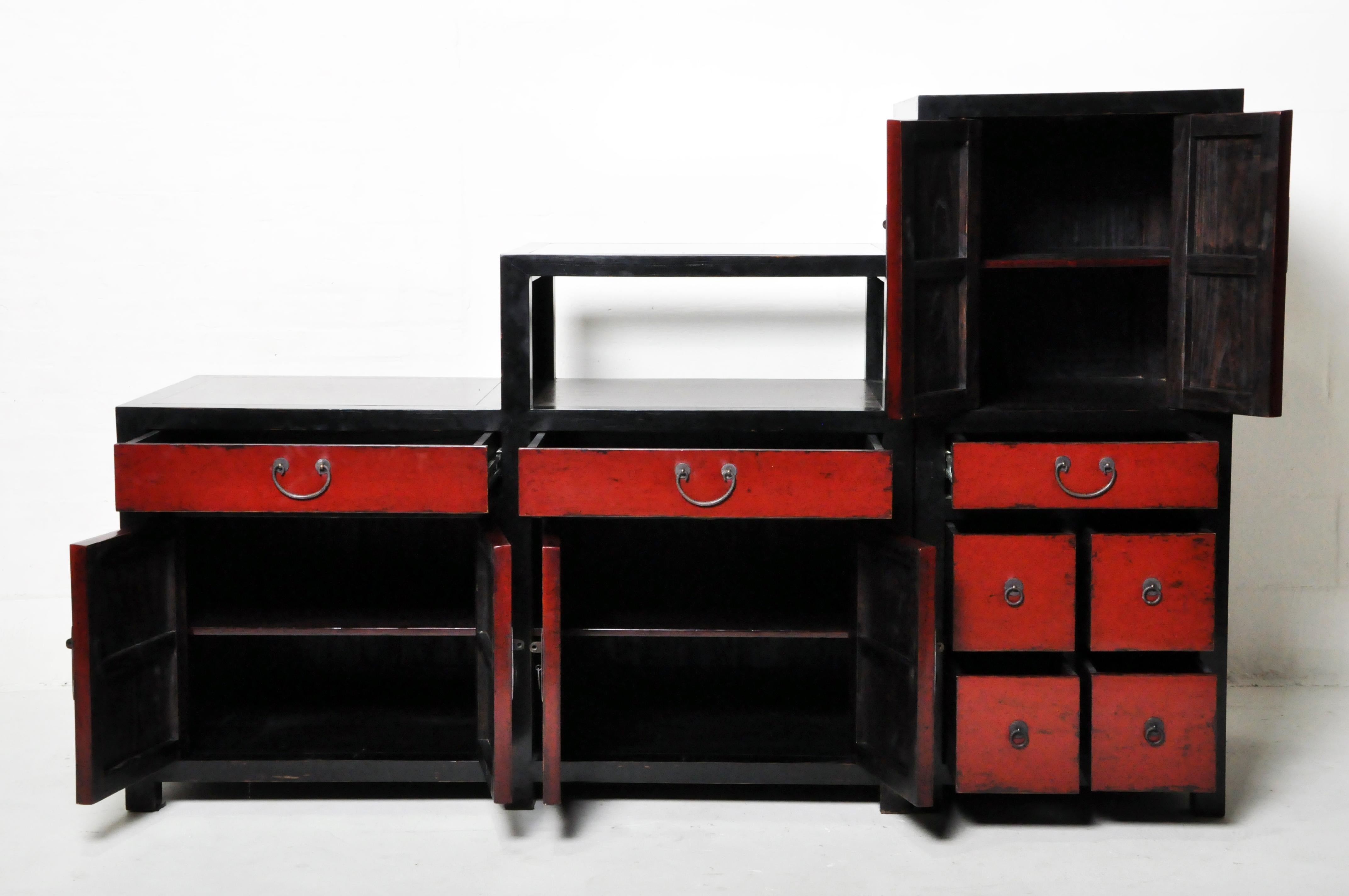 A fine custom-made storage and display cabinet. This piece is made from elmwood and covered in red and black lacquer. It is two-sided and made from two segments, for ease of movement. A glass shelf allows the display of small objects.
  