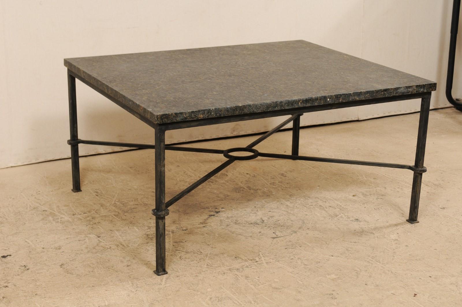 A custom American coffee table with honed granite top. This modern designed coffee table features a honed granite top raised upon a black iron base comprised of four straight legs, which are supported by an x-style stretcher with an o-shaped ring at