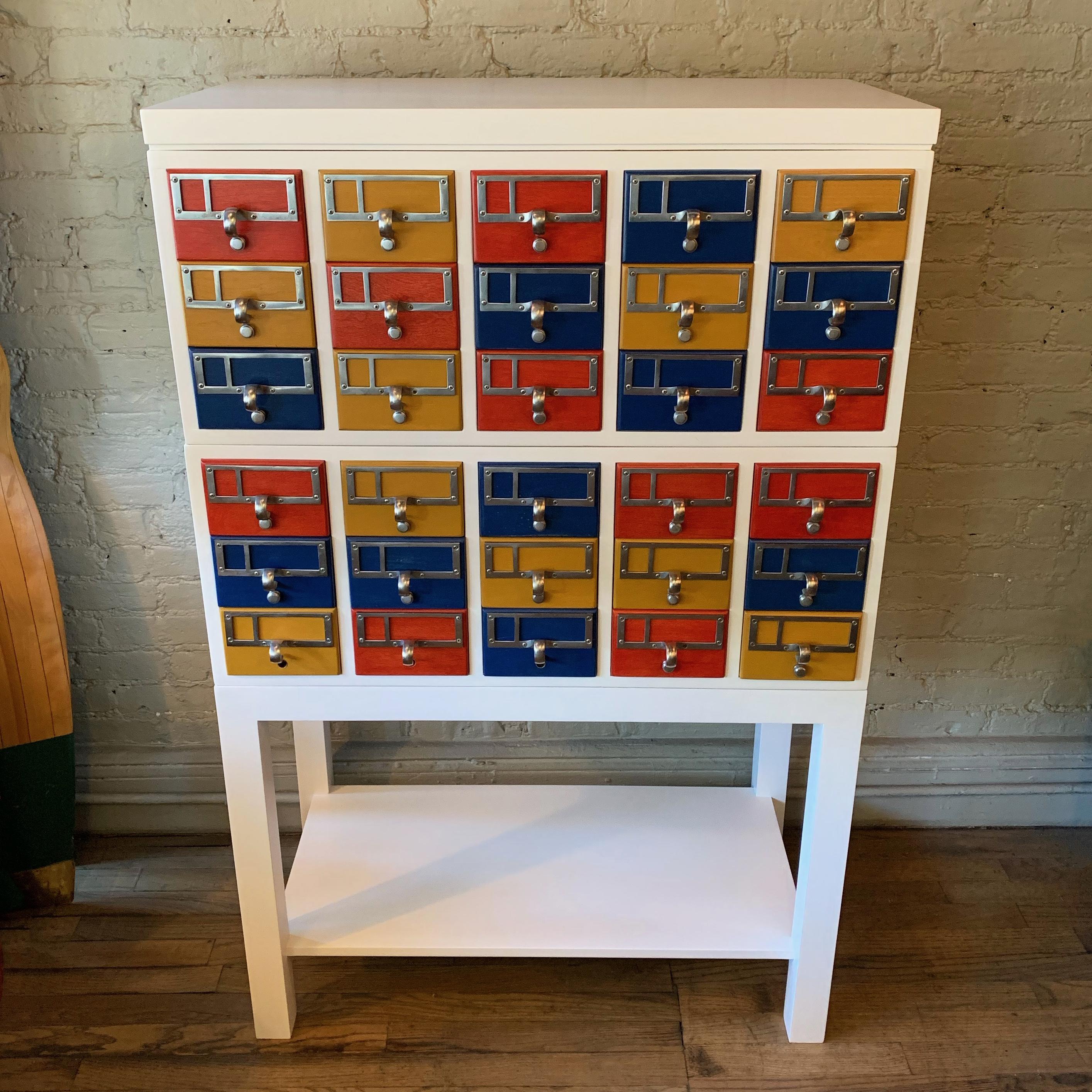 Modular, midcentury, maple, library, card catalog cabinet is custom finished in white matte lacquer with contrasting, color block drawers that measure 5.75in w x 4in ht x 14.5in d with aluminum hardware. The top cabinets measure 30 inches height and