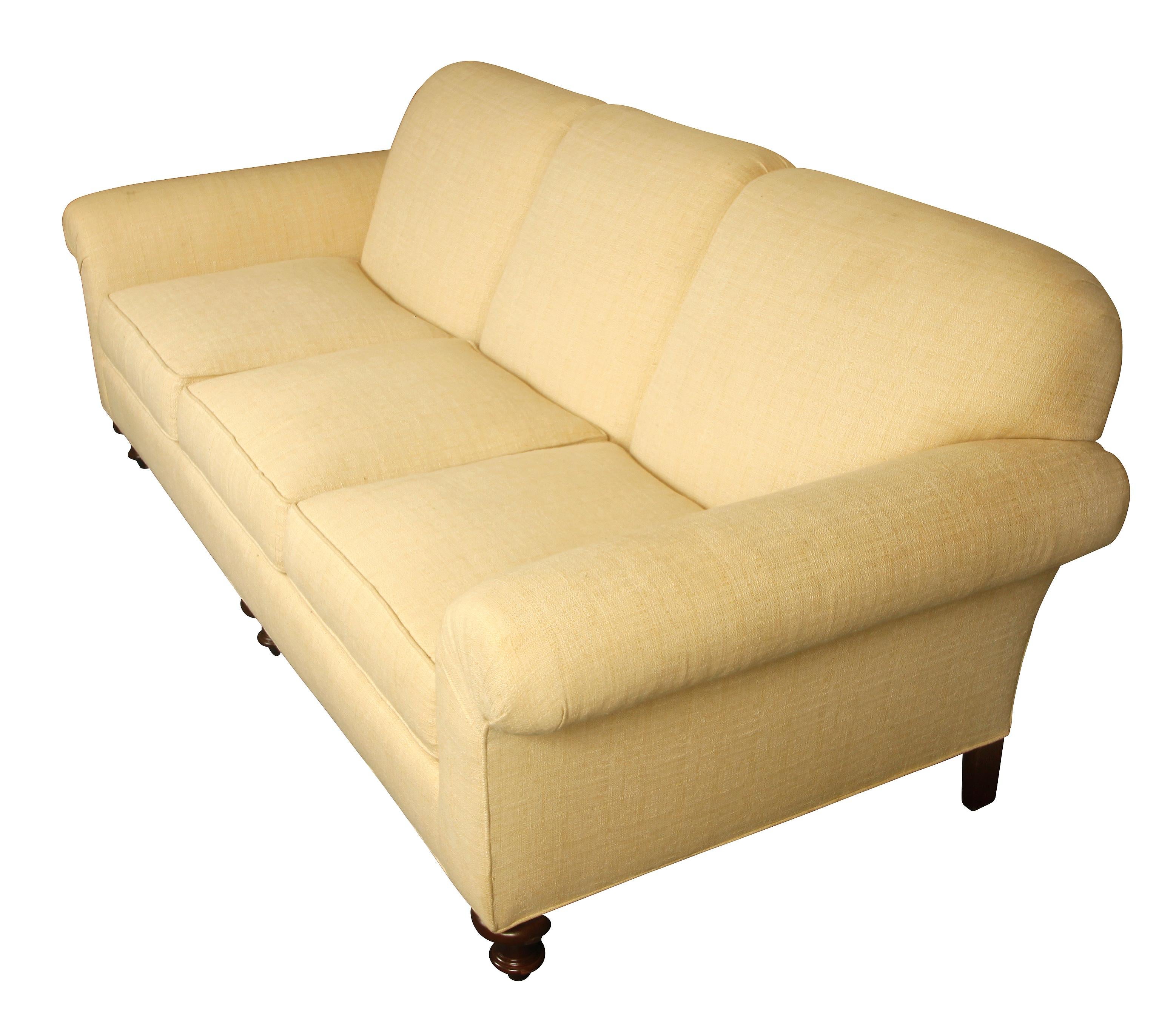 Custom cotton, upholstered roll arm sofa in cream linen with rounded wood feet. Classic piece, comfortably seats three with removable cushions.