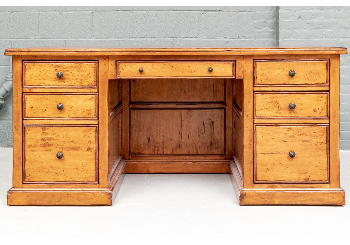 A very well made desk with finished back. In a honey tone wood with an antiqued finish with intentional dings. Classic lines with three apron drawers and two short drawers over file drawers on each side. All with carved darker wood knob pulls.