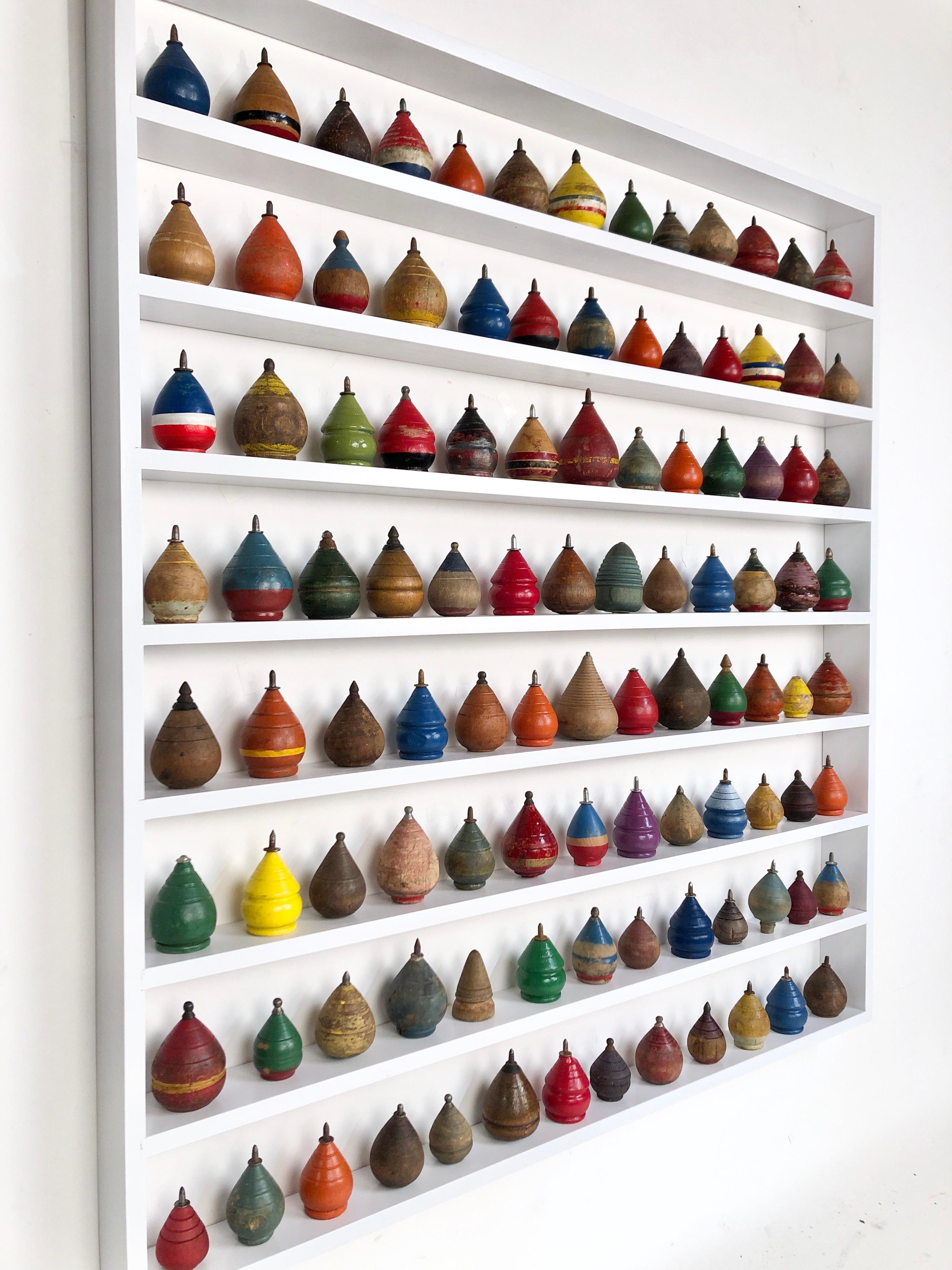 A custom built white painted maple shadow box containing 104 antique wooden spinning tops of various shapes, colors and sizes. Can be arranged any way you like. These antique spinning tops are circa 1890-1950. The custom built frame is 30