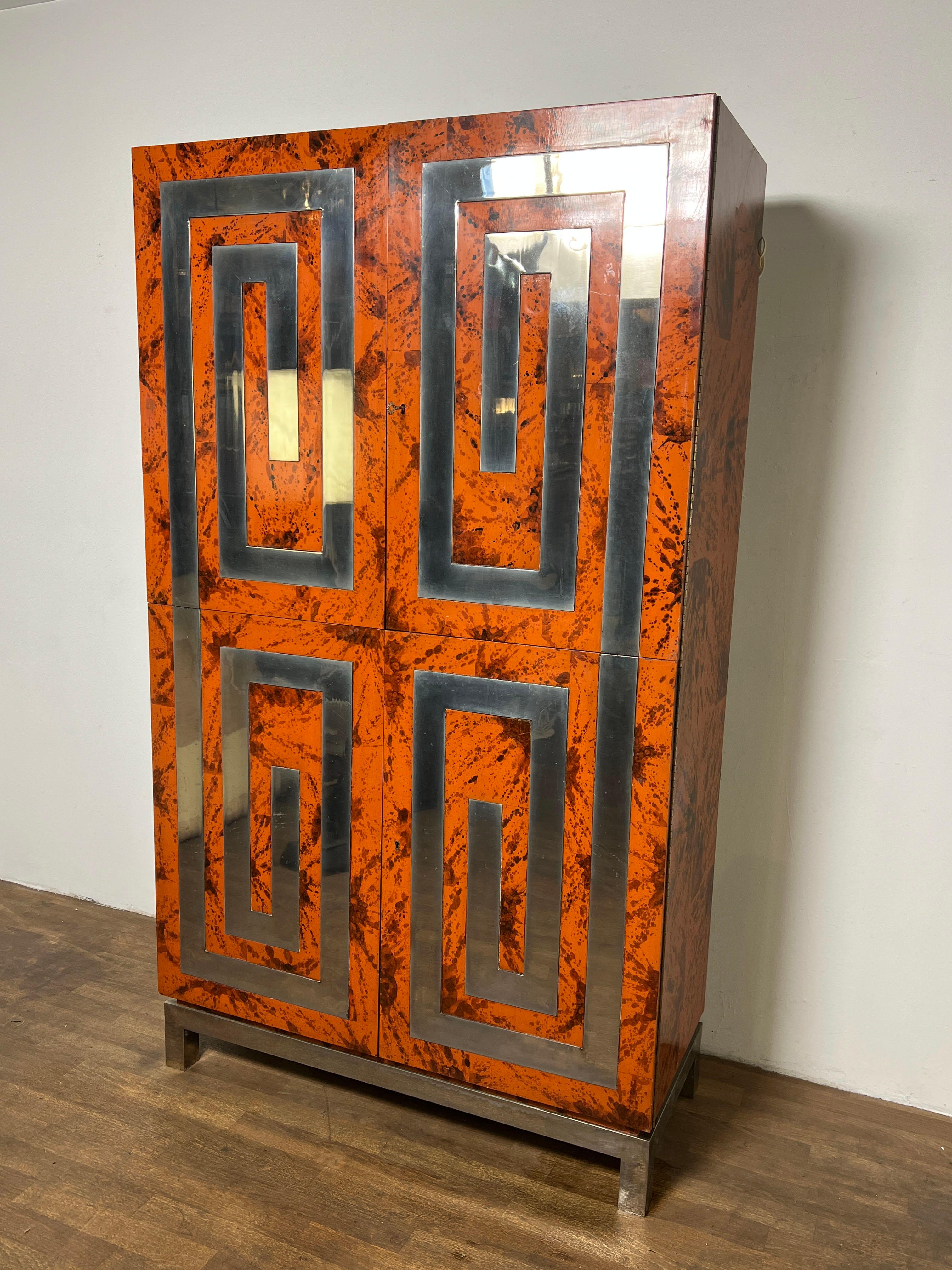 A unique custom made lighted dry bar or media cabinet, ca. late 1970s, in faux tortoiseshell lacquer with a Greek key motif of inset polished aluminum panels. Features a lighted upper cabinet for bottle and glassware storage with an expandable
