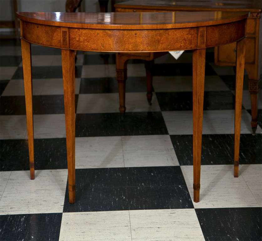Veneered in the finest walnut burl, this demilune / console has straight-grain crossbanding and inlays of satinwood. The lightly tapered legs are a Classic look, but allow this table to bridge many styles. The clean lines could work in a modern