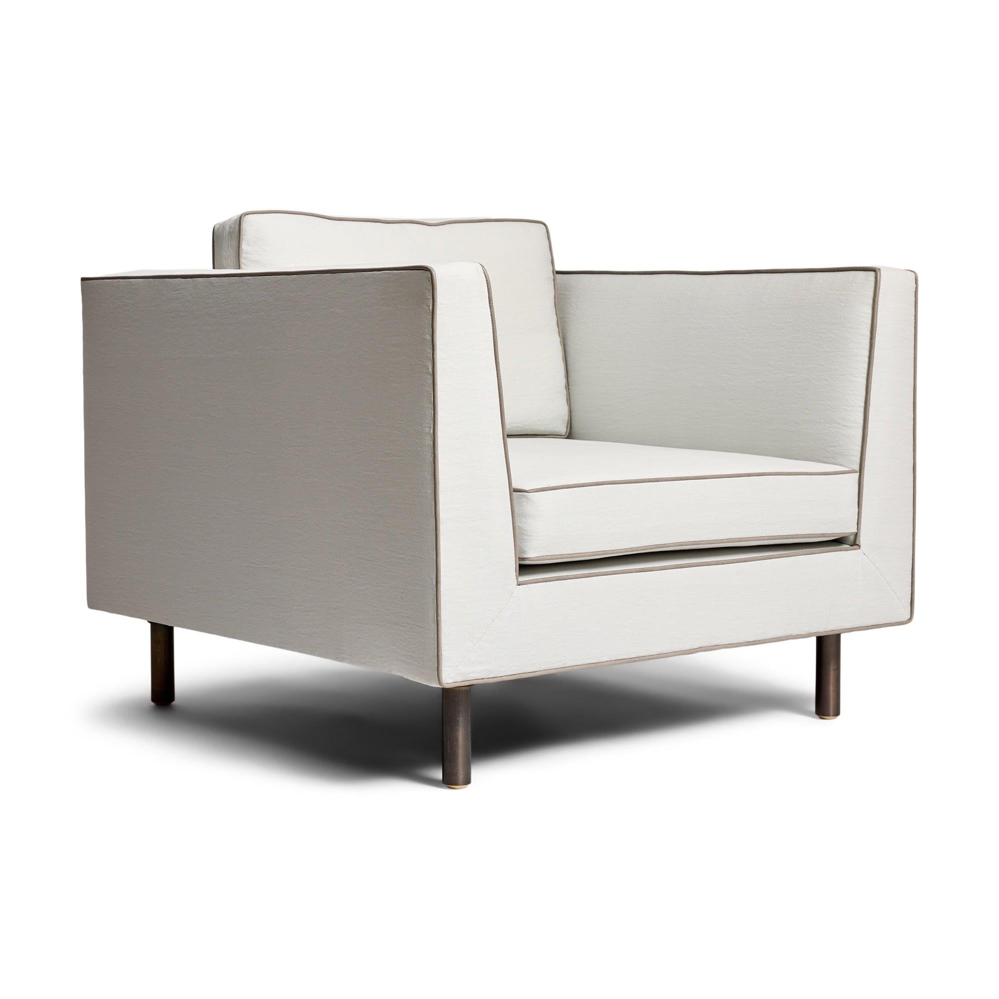 Una poltrona lounge con braccioli, su solide gambe rotonde in bronzo, con tessuto bianco e rivestimento in pelle.