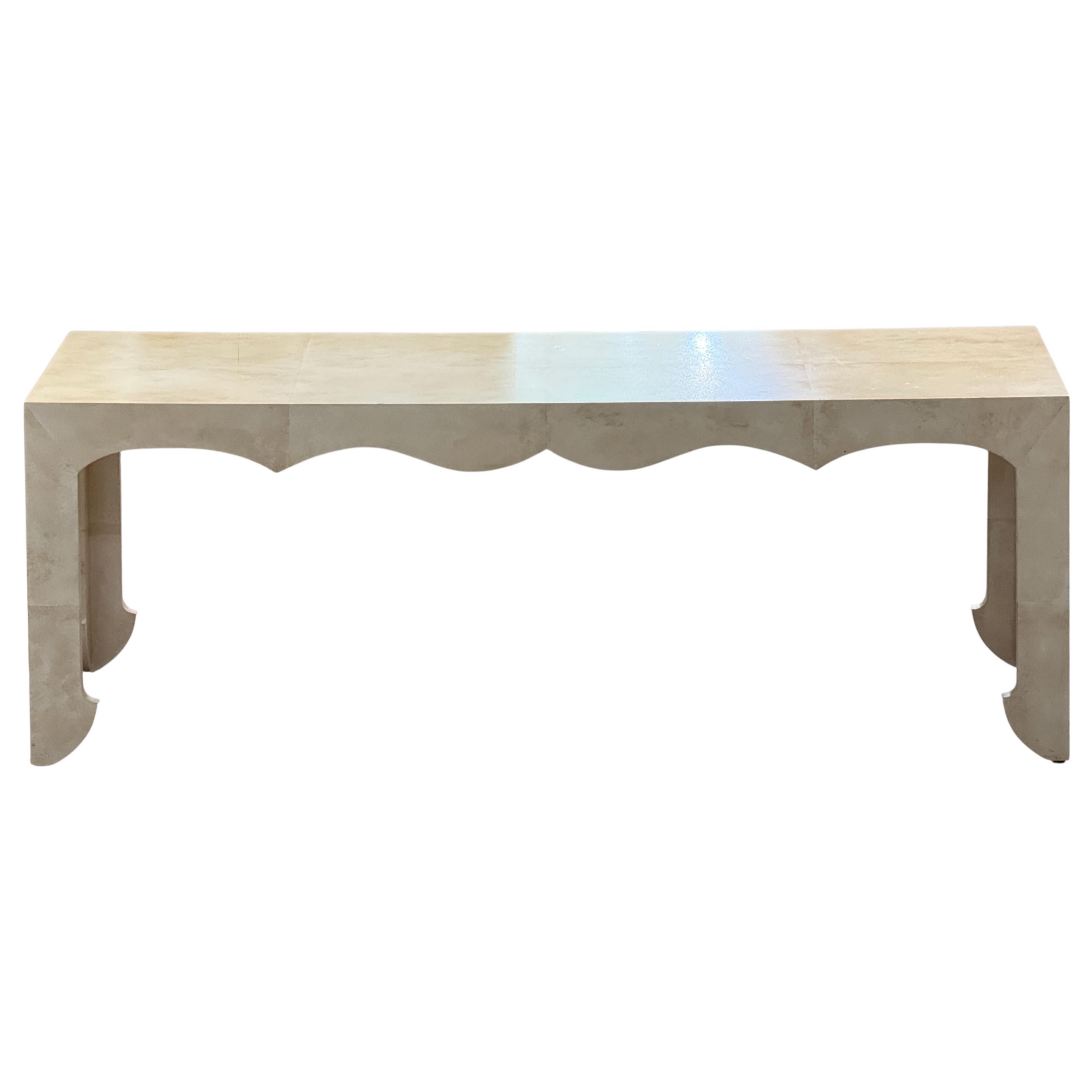 This custom cocktail table features a soft faux parchment finish over clean architectural lines. The shaped apron and subtly flared legs add tailored detail to the minimalist silhouette, balancing form and texture with quiet sophistication.
