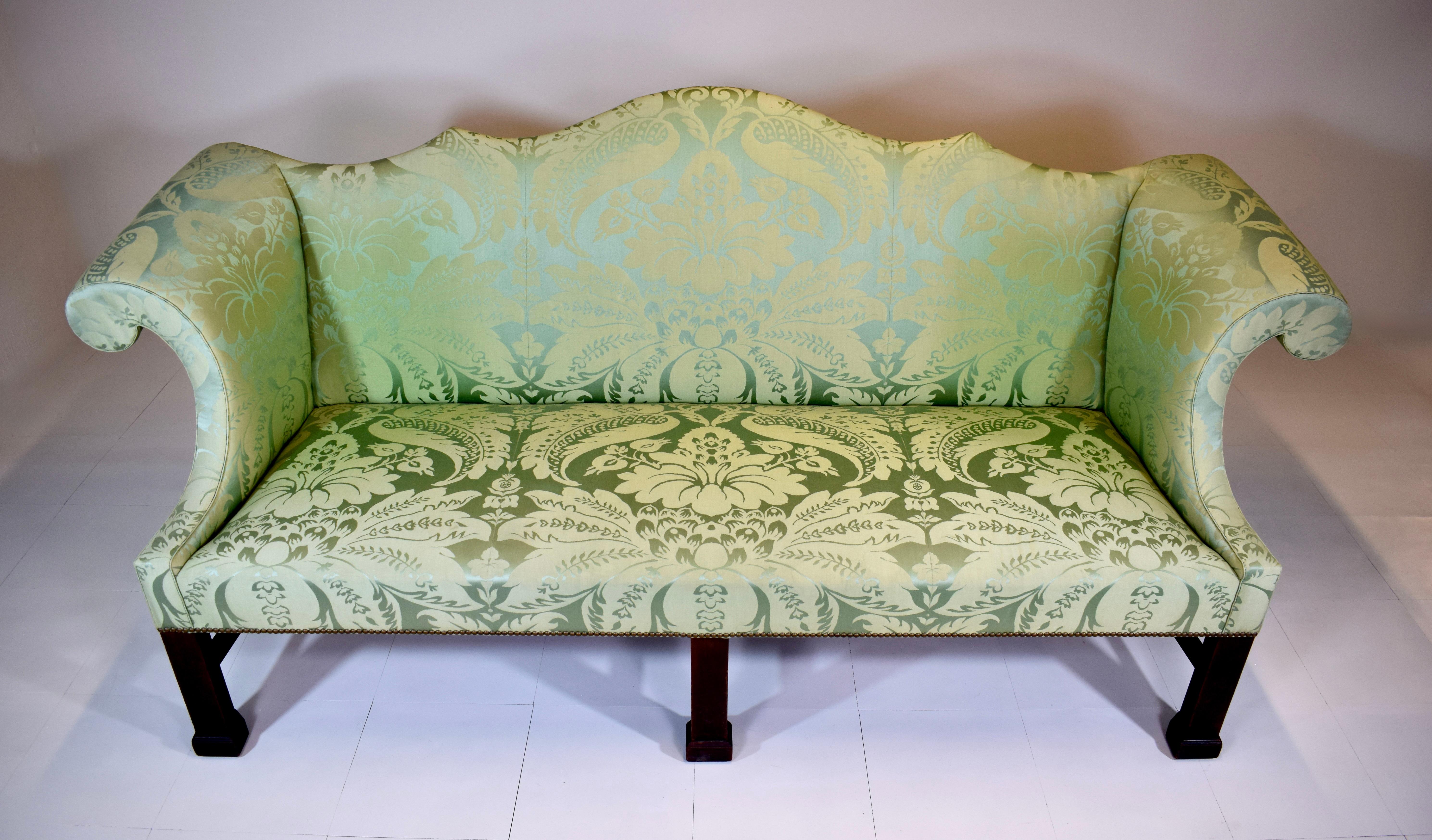 A spectacular Custom George III Mahogany Camel Back Sofa upholstered in exquisite Damask silk accentuating a well drawn camel back silhouette, gently curved scrolled arms, and straight legs united by triple H stretcher supports with block feet.