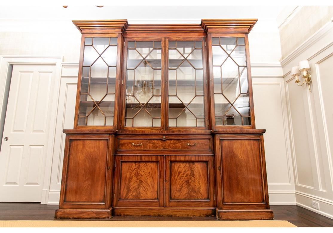 With a carved overhanging top over a three-part step back case. Each section with mullioned wavy glass doors and lined in ecru moire. A total of eight adjustable shelves with carved edges for the side sections. The center with three long