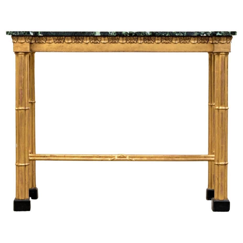 The shaped form with extended square corners and green marble top. A gilt wood frame with carved leafy frieze with beaded edge. Raised on clusters of bound cylinders for the column form legs with similar clusters of bound cylinders for the H