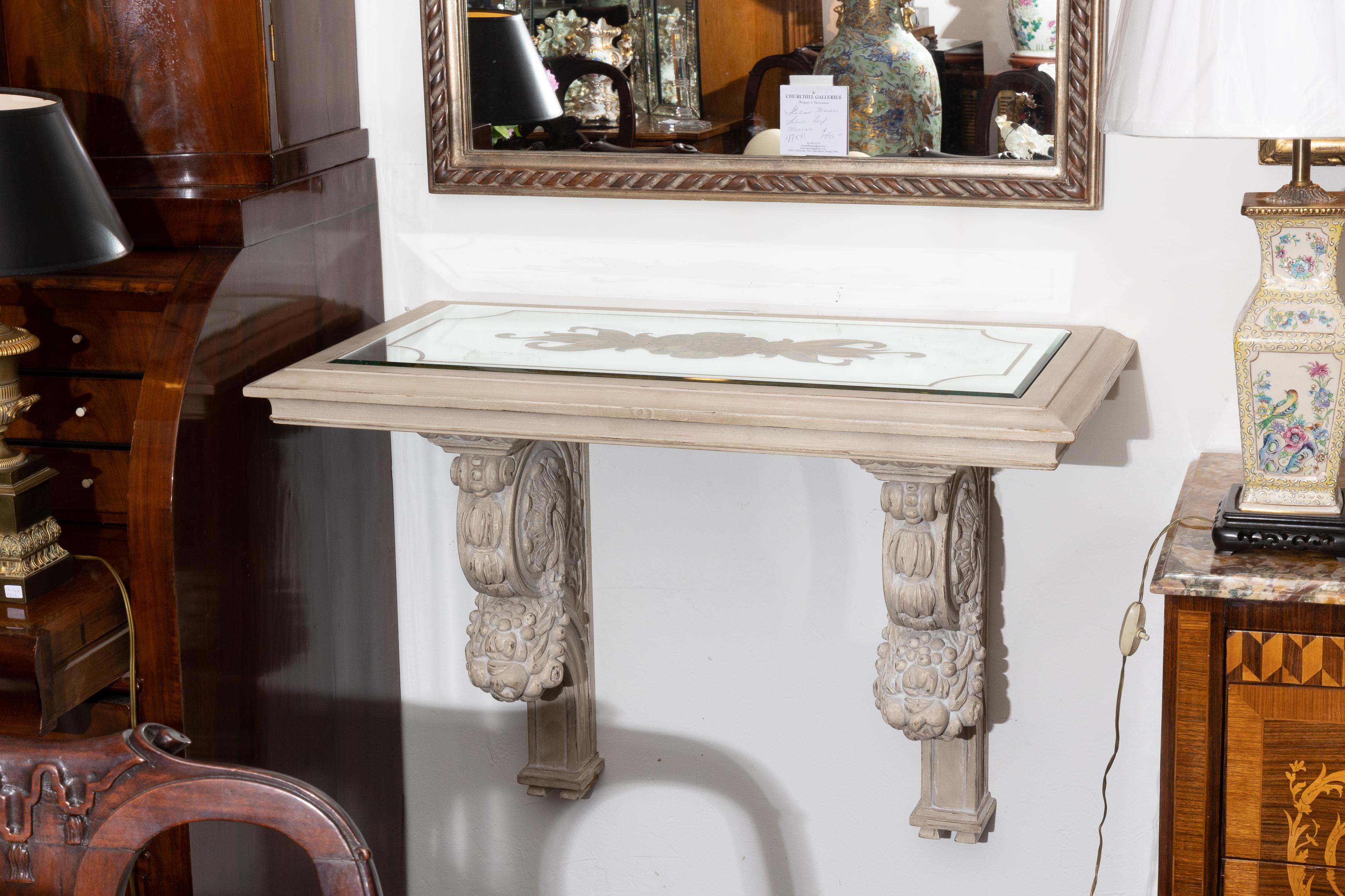 This is one of a set of four hand carved hanging consoles, lightly white-washed to highlight carved details of fruit and ornamental features. The top of each console has an etched mirrored-inset top containing a gilded central ornamental design,