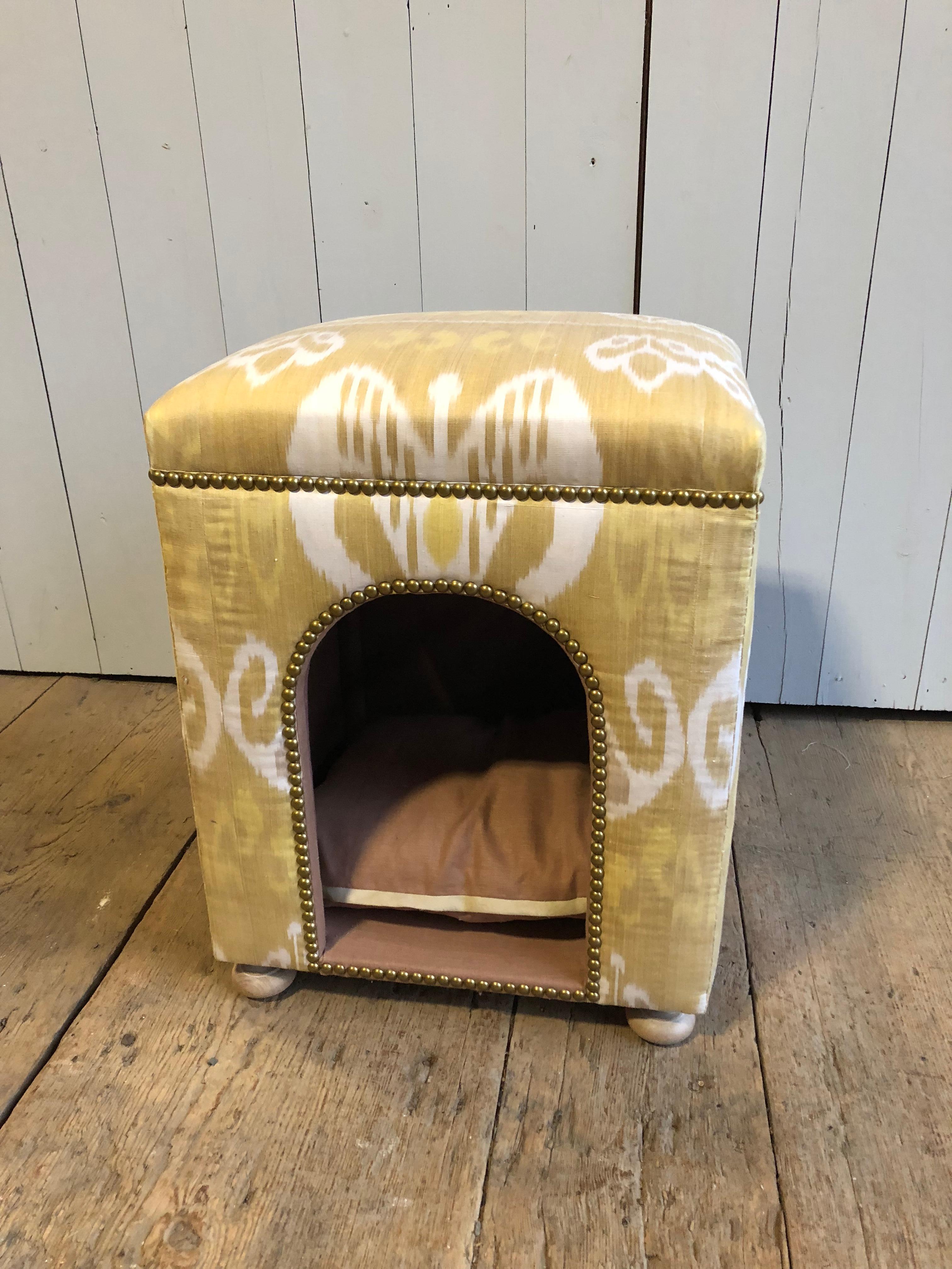 A custom dog bed upholstered in handwoven silk Ikat fabric, the top padded and at seat height to double as a stool. Brass decorative nailheads and turned wood feet.
Hand-holes in each side for portability. Originally retailed by Lillian Williams in