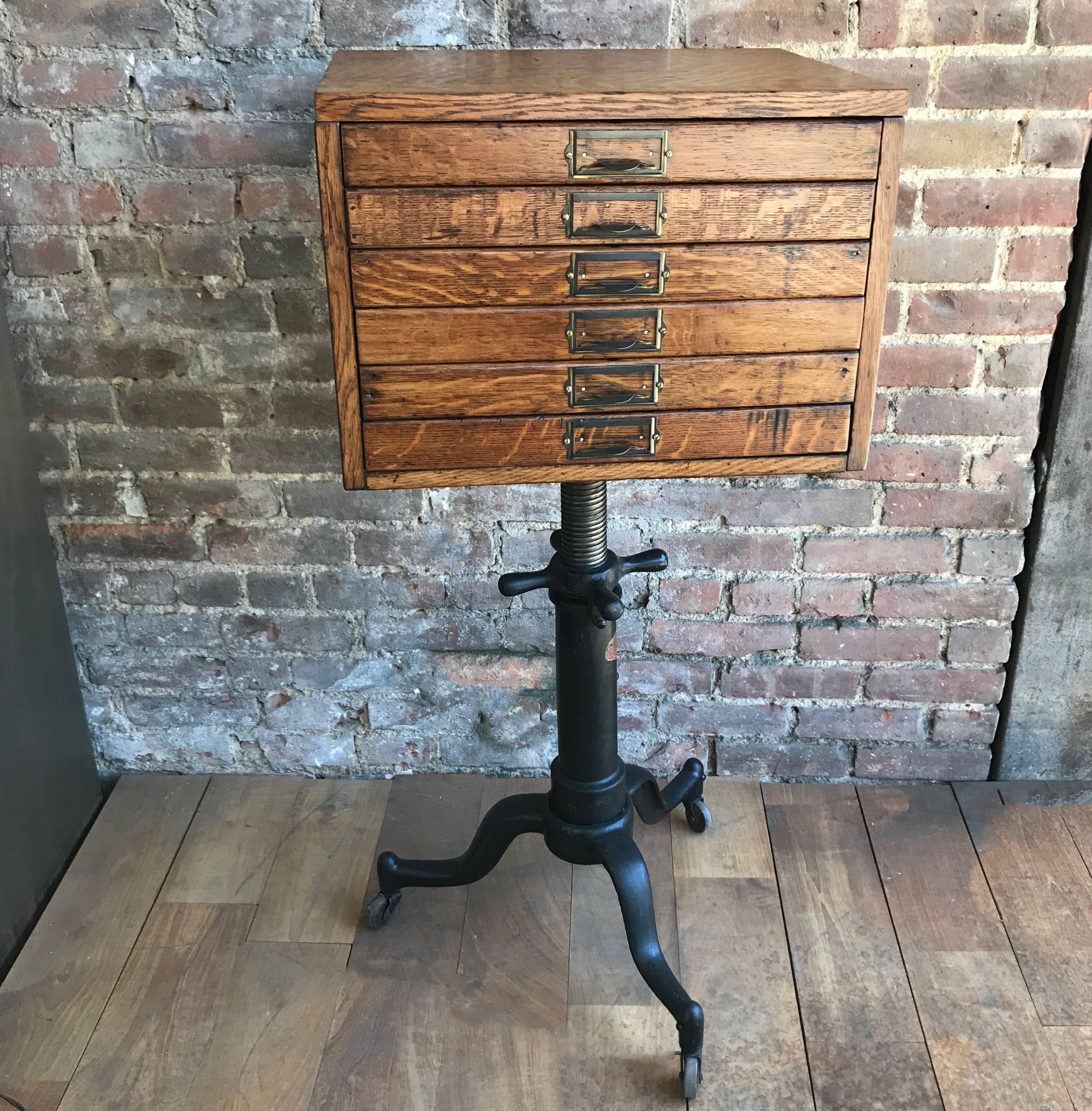 Custom, industrial, early 20th century, quarter sawn oak flat file cabinet with brass pulls mounted atop a height adjustable, cast iron pedestal base. The cabinet height measures 13.5 inches and the drawer interiors measure 16 inches wide x 10.5
