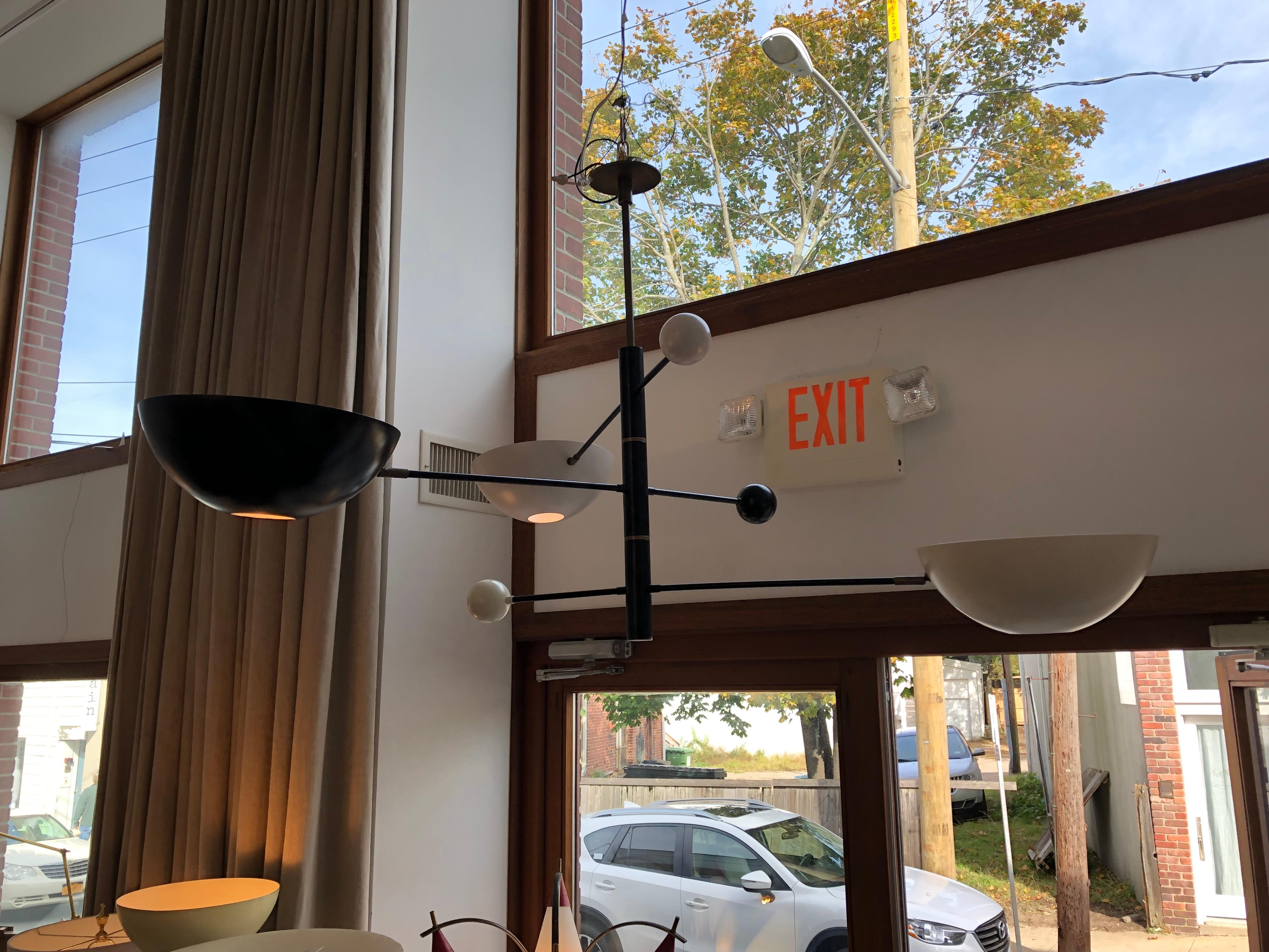 Vintage style three arm floating chandelier, inspired by Italian midcentury lighting designs this chandelier features three pivoting extended arms radiating from a center column with alternating black, cream and white metal shades and matching ball
