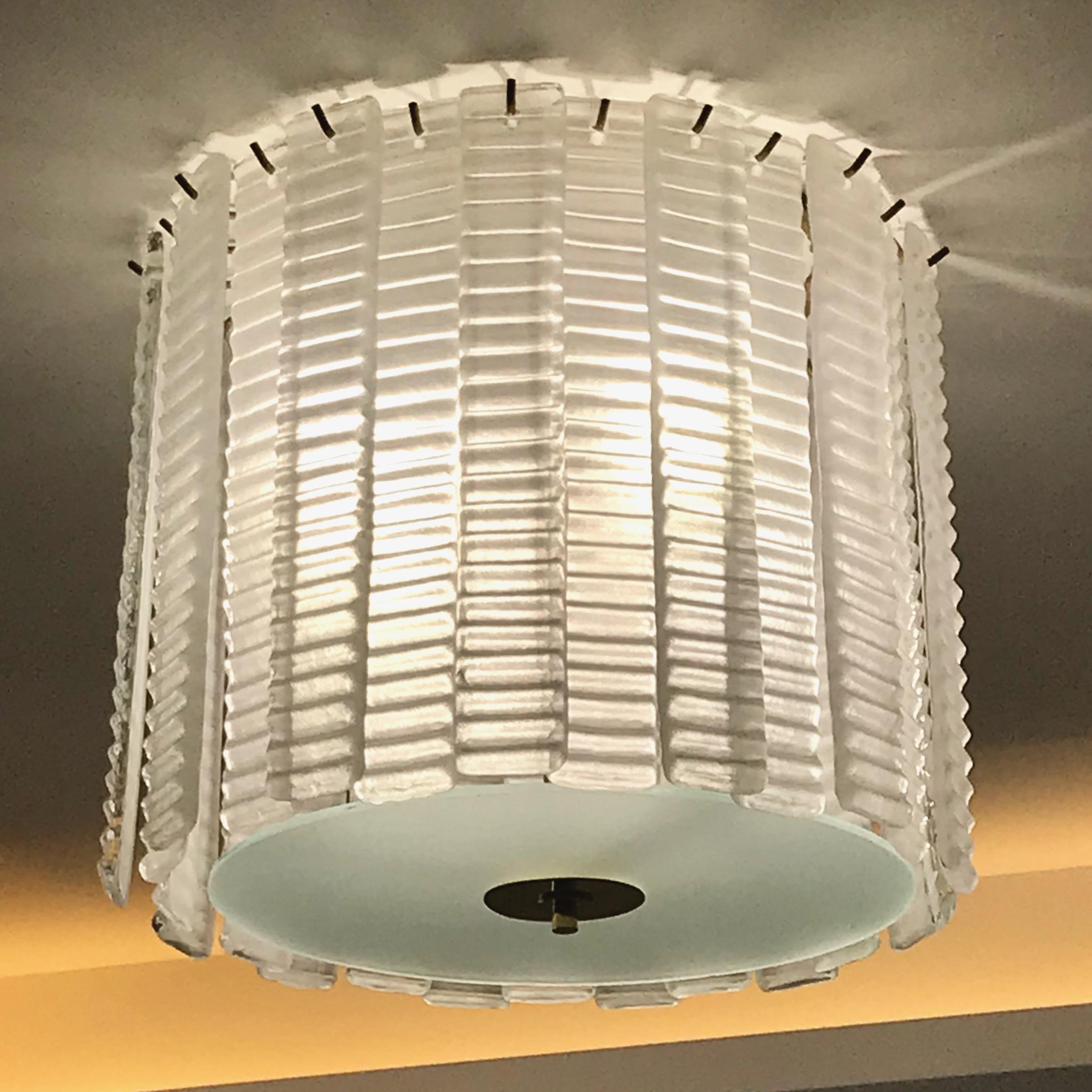 Cosulich Interiors custom design bespoke light fixture in frosted crystal clear murano glass, composed of straight strings with a sensual wavy pattern enclosing a glass circle with brass finial in frosted glass to diffuse the light source. The