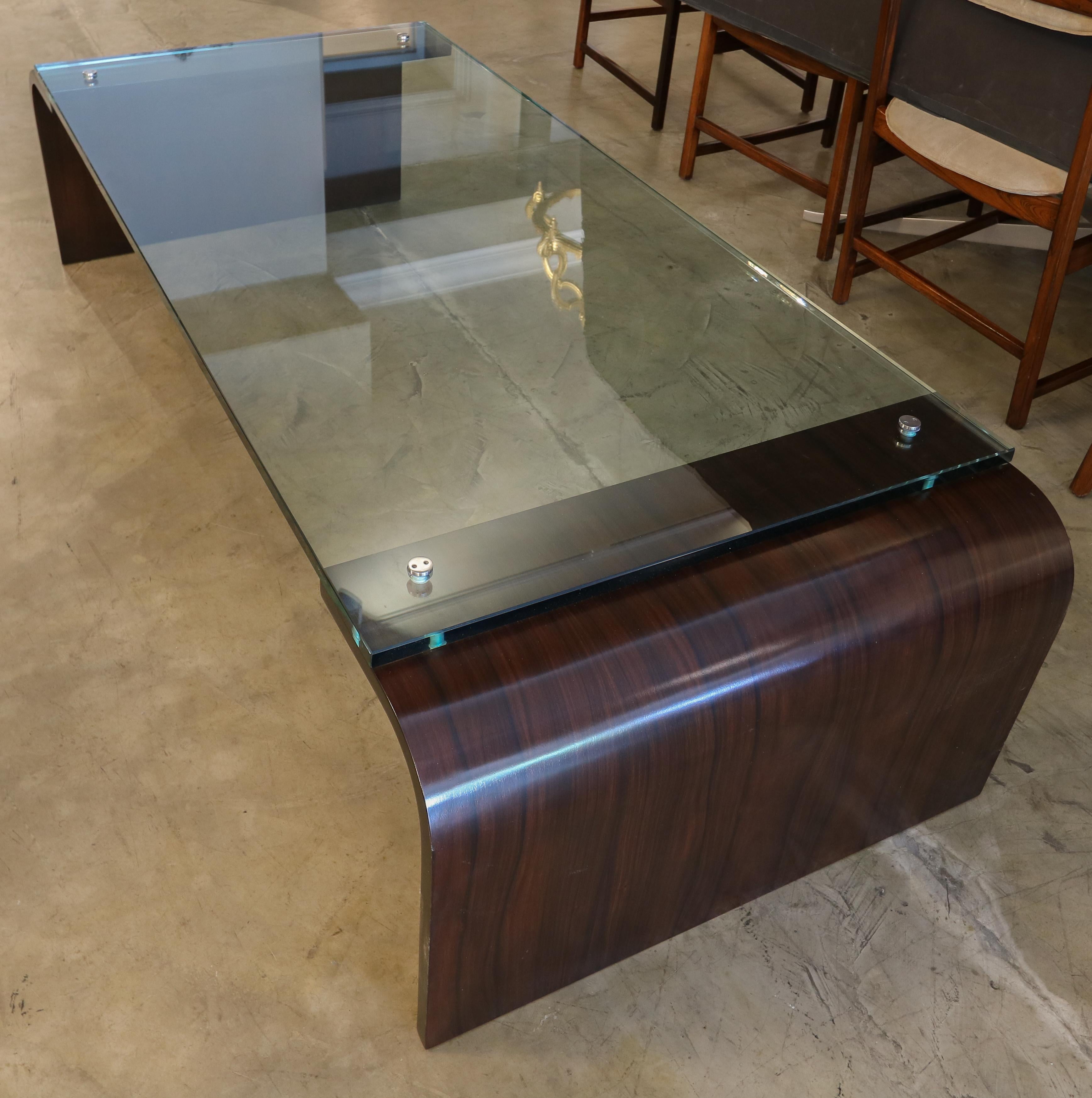 Custom coffee table with curved waterfall rosewood ends and glass top attached with handmade decorative metal screws.  Made in Los Angeles by Adesso Imports.

Can be done in different sizes and finishes.