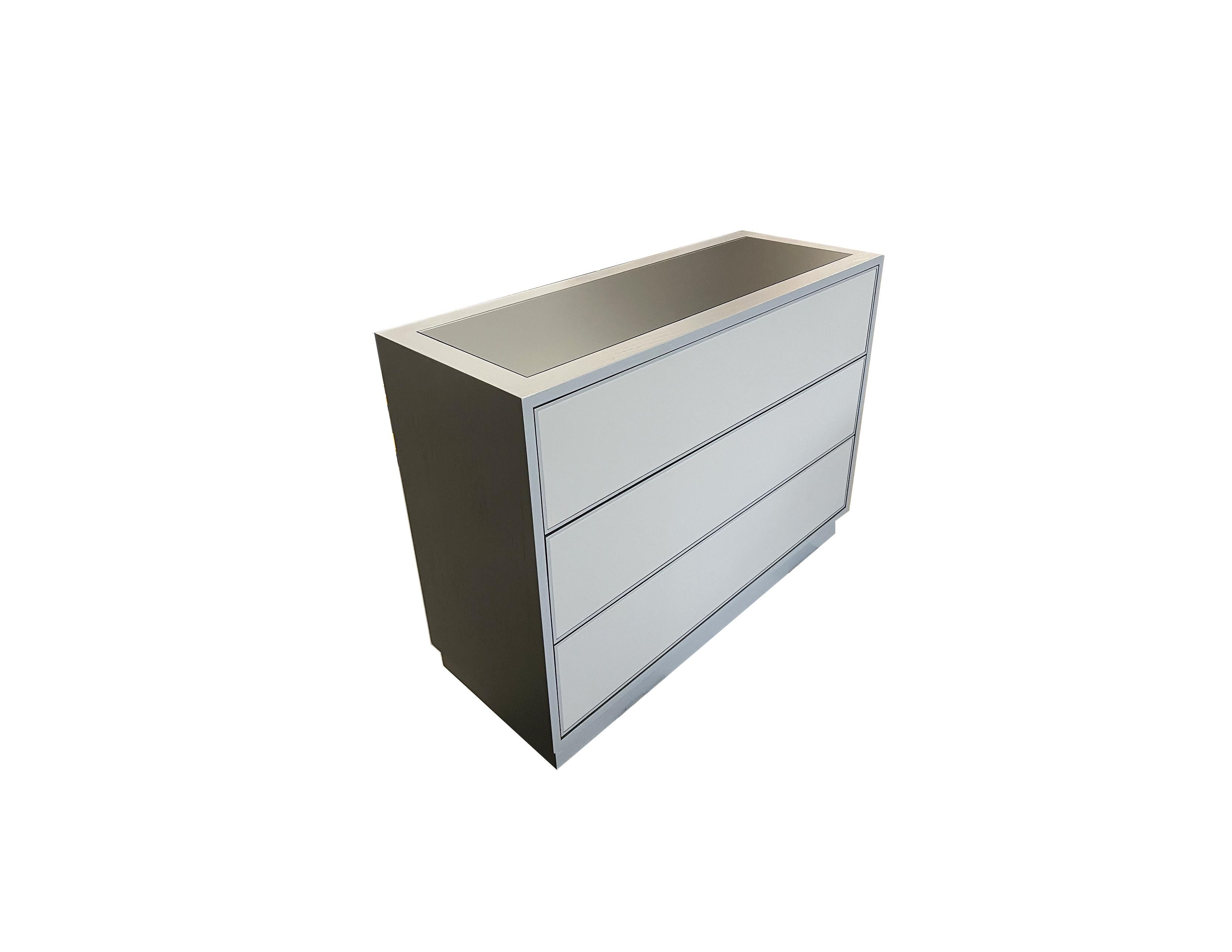 Our custom chest of 3 drawers by Ercole Home is made up of three touch latch drawers. The faces of each of these drawers are covered in a custom grey leather with a 1/4