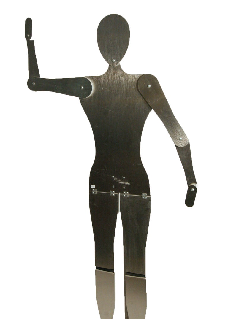 This custom made mannequin is rendered in brushed aluminum and rests on an aluminum base. The figure is adjustable in a variety of positions and may also be raised and lowered to various heights. There are casters along the back for easy mobility.