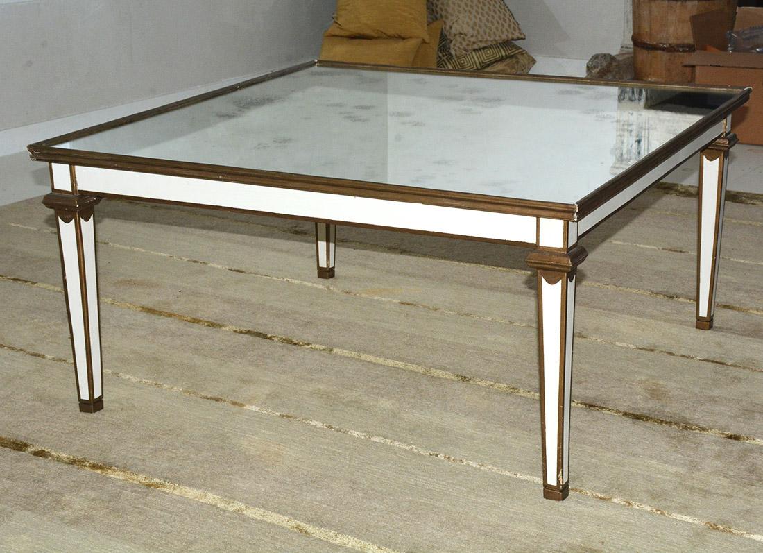 Painted white with gilt trim, the neoclassical coffee or end table features a mirrored top and tapered legs. The styling lends itself to almost any room with either a traditional, classical, neoclassical or modernist contemporary styling. Other