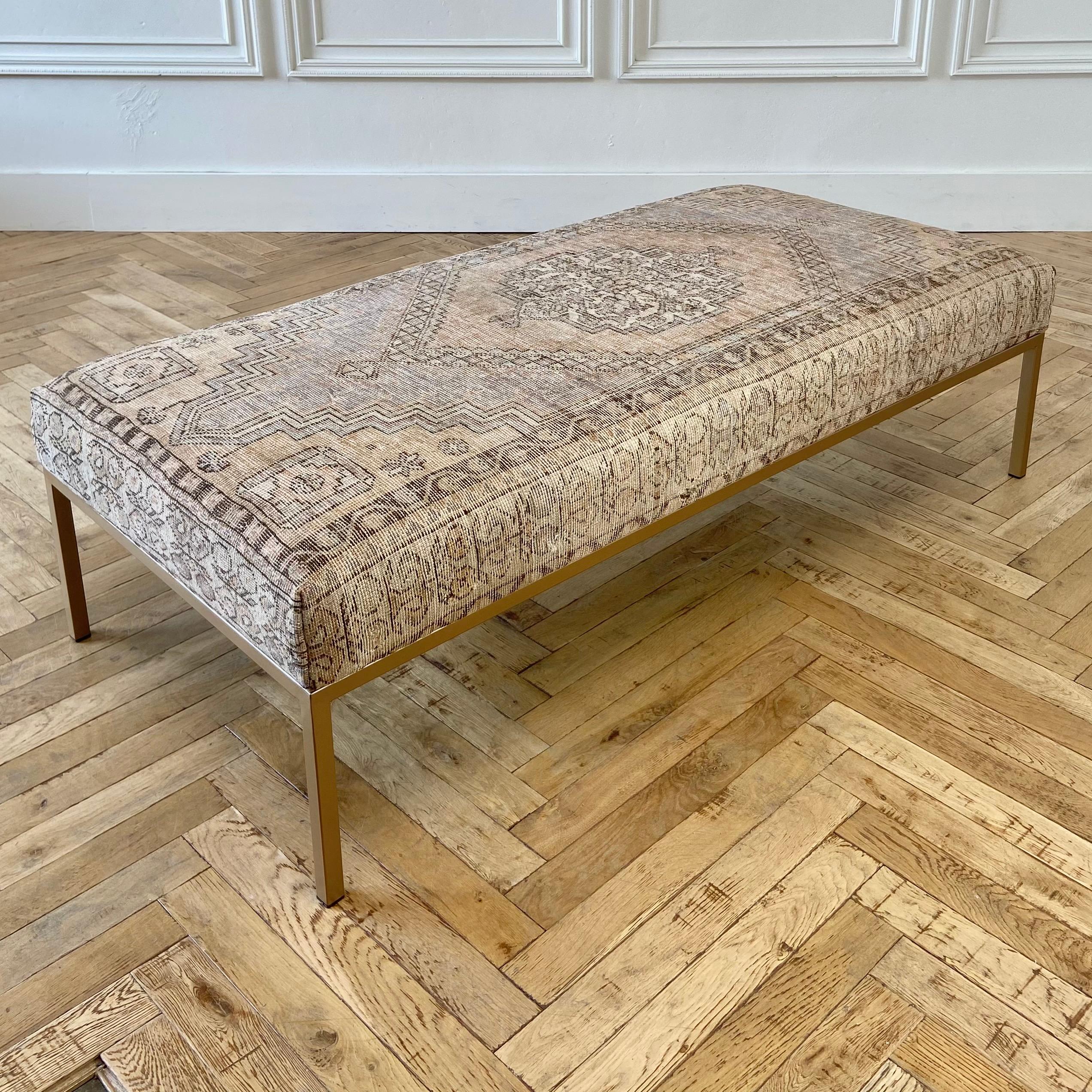 Custom made iron cocktail ottoman with vintage wool Turkish rug.
Frame is metal in a satin antique brass finish. Upholstered top in an antique wool turkish rug, in faded salmon, taupes, creams, blues, and brown tones. A firm foam topper makes it a