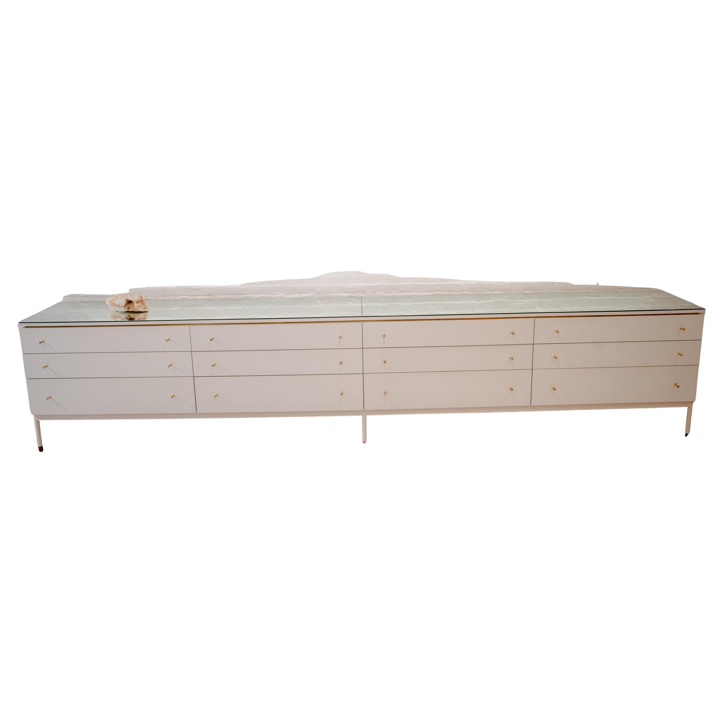 This custom-built long credenza provides makes for elegant storage and display in a living or retail space.

With 12 wood drawers finished in a crisp white paint and accented with brass hardware and details, this piece offers ample storage.