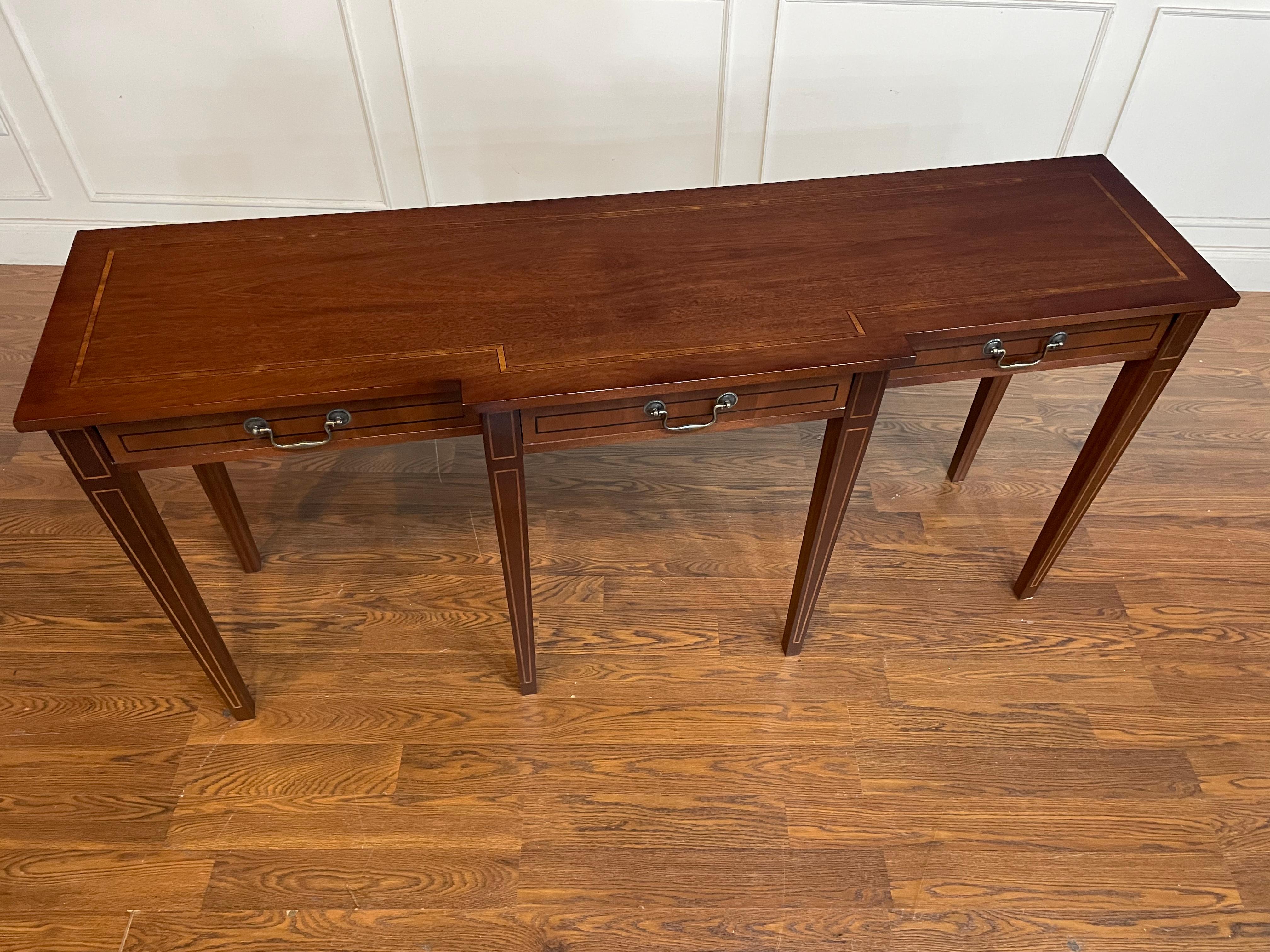 This is our Hepplewhite style mahogany console table. It features classic Hepplewhite styling with square tapered and inlaid legs, a cathedral mahogany top with Movingue inlay, inlaid drawer fronts with traditional dovetailed oak drawer boxes and