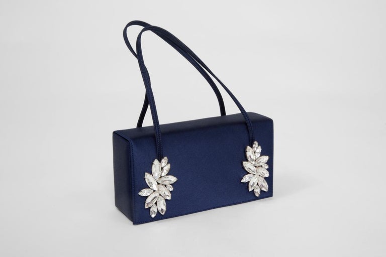 Enhance your evening looks with this refined custom made Renaud Pellegrino bag. Made from dark blue satin silk, each end of the handles is decorated with different sizes of Swarovski oval crystals. Matching blue satin silk interior is featuring one