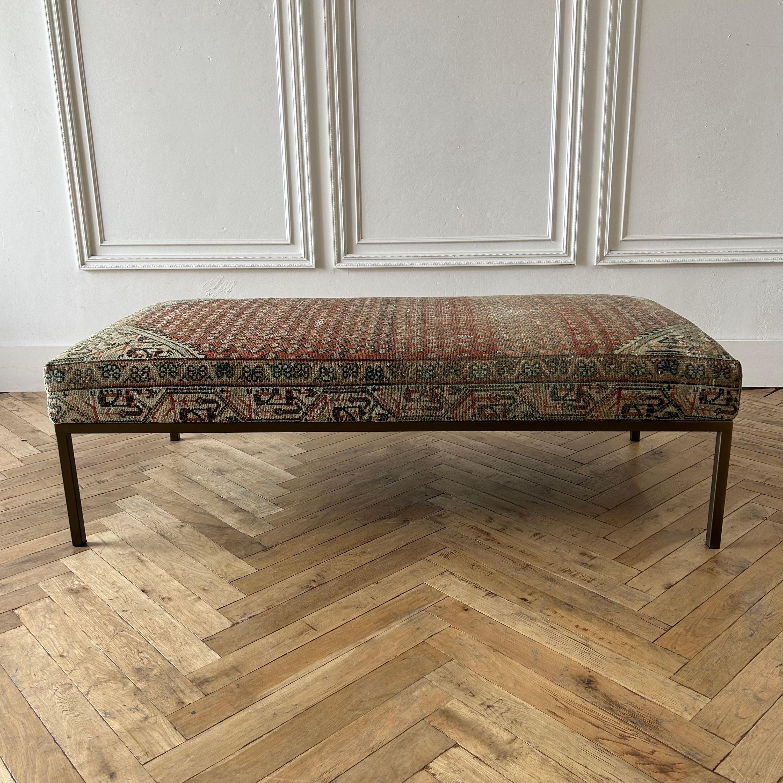 Custom Made bench ottoman by Bloom Home Inc.
Size: 60”w x 30”d x 18”h
Custom made metal base, and powder coated in a dark iron bronze finish.
The upholstered top is from an antique or vintage turkish rug.
Color: faded brick / gray / off white /