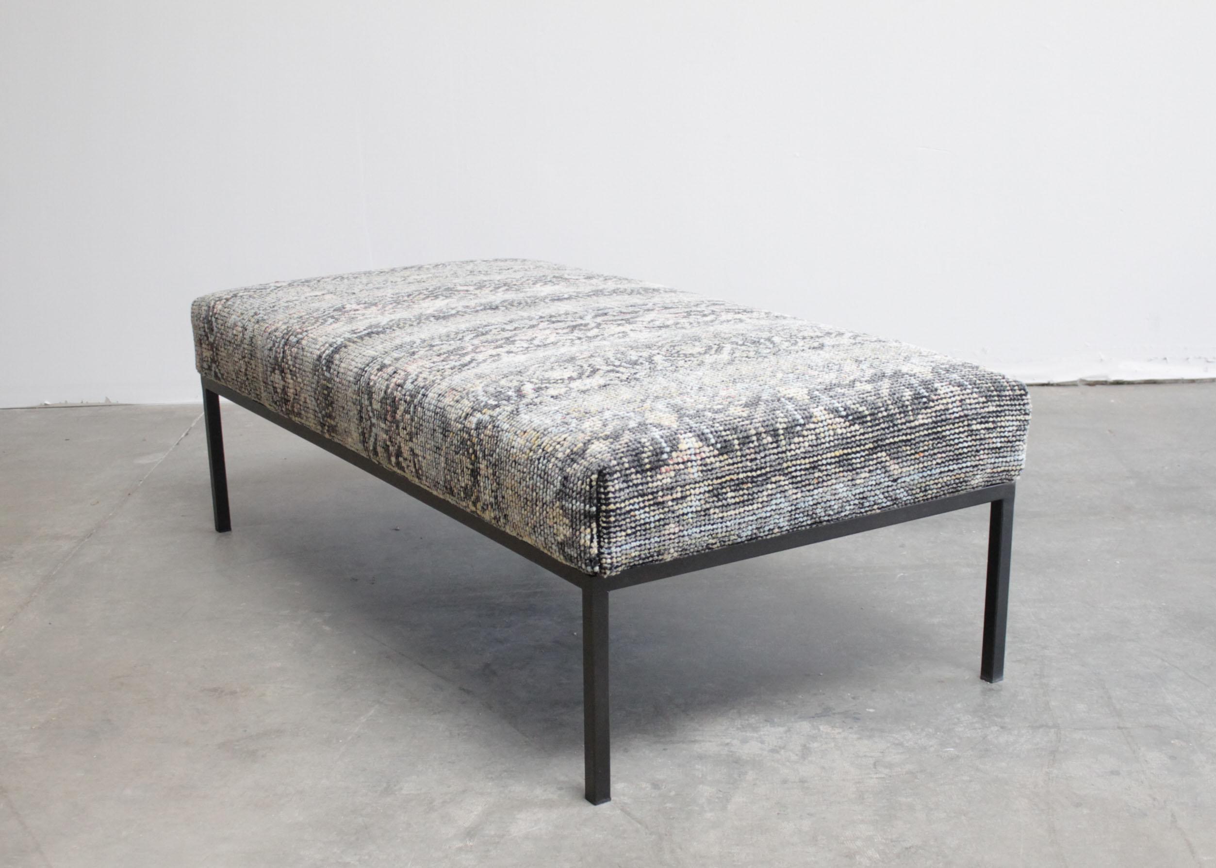Custom made iron upholstered cocktail table bench ottoman.
The base is a custom finished iron base, with a vintage style rug upholstered top. The very durable top is a heavy weaved wool. Dark grey, light grey, tan, indigo, blue, faded reds, and off