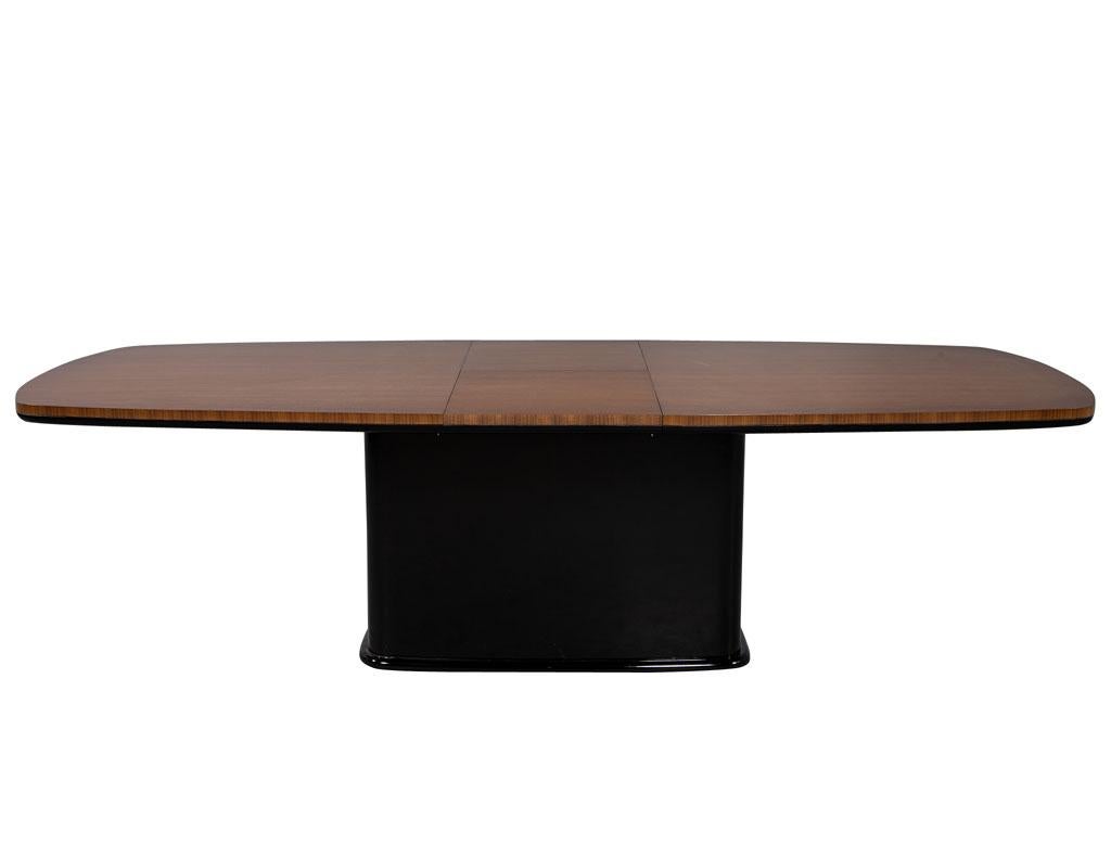 Carrocel custom Mid-Century Modern inspired dining table. Featuring rectangular pedestal with rift cut vertical walnut and bottom molding in black. Finished in a natural walnut satin flat finish. This table has a butterfly leaf that can be stored in