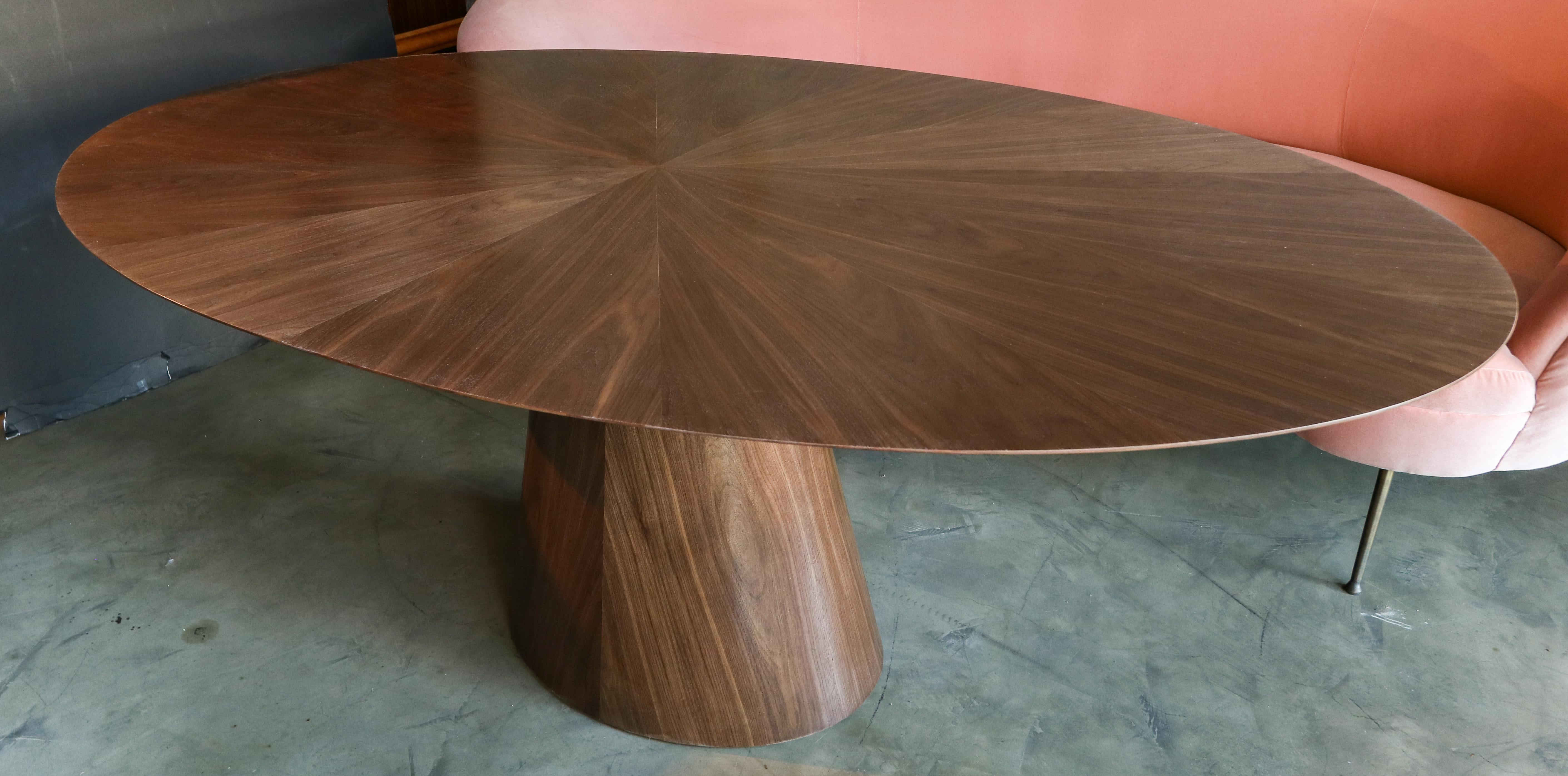 Custom oval dining table with pedestal leg made in American walnut.  Made in Los Angeles by Adesso Imports.

Can be done in different woods, finishes and sizes.
