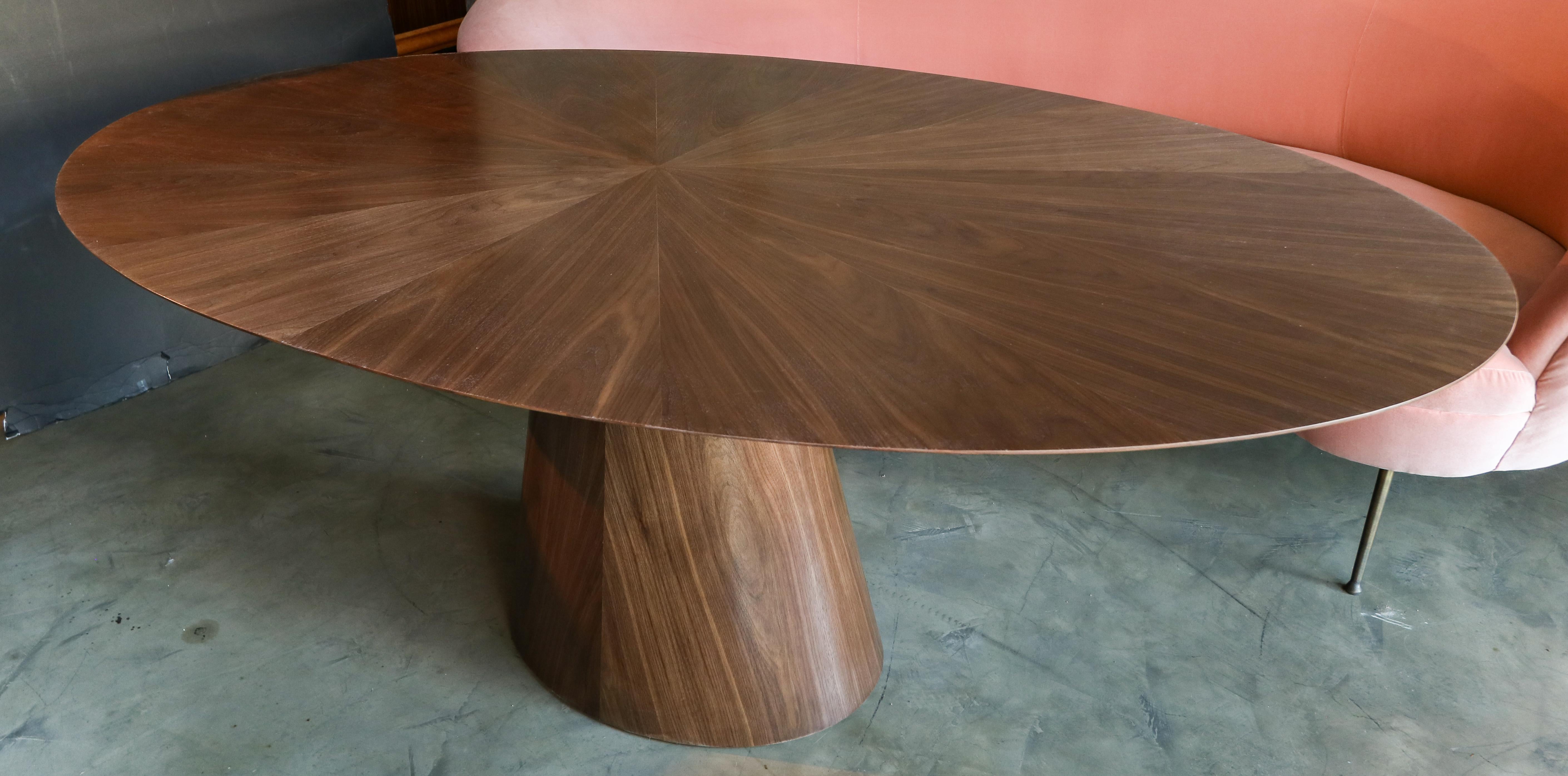 Custom oval dining table with pedestal leg made in American walnut.  Made in Los Angeles by Adesso Imports.

Can be done in different woods, finishes and sizes.