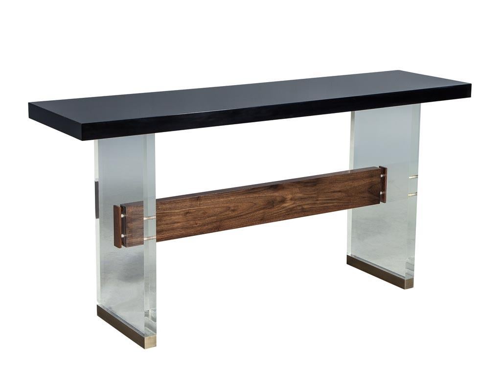 Custom modern acrylic black lacquer and walnut console by Carrocel. This Carrocel custom-made acrylic console features a walnut trestle with a polished lacquer top and is finished off with classic brass feet. This piece accentuates the stunning wood