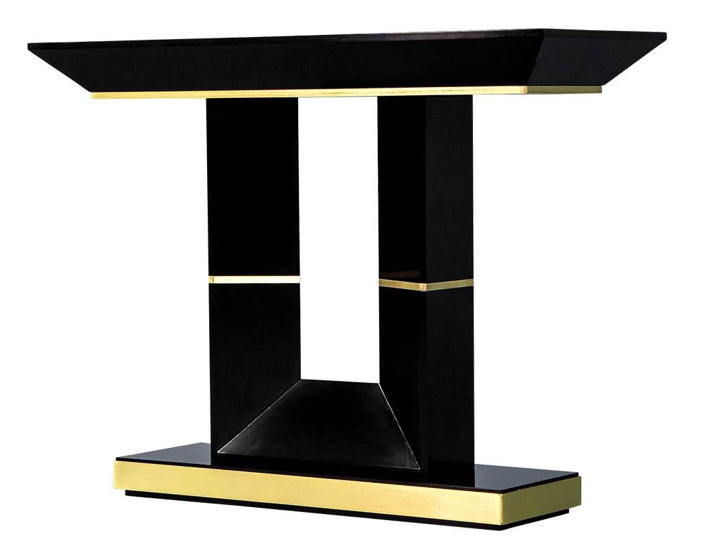 Custom modern black lacquered console table by Carrocel. Handcrafted here in Toronto, Canada and ready to ship. Art Deco inspired design, finished in hand polished black lacquer accented with brass trim under the apron, surrounding the base and