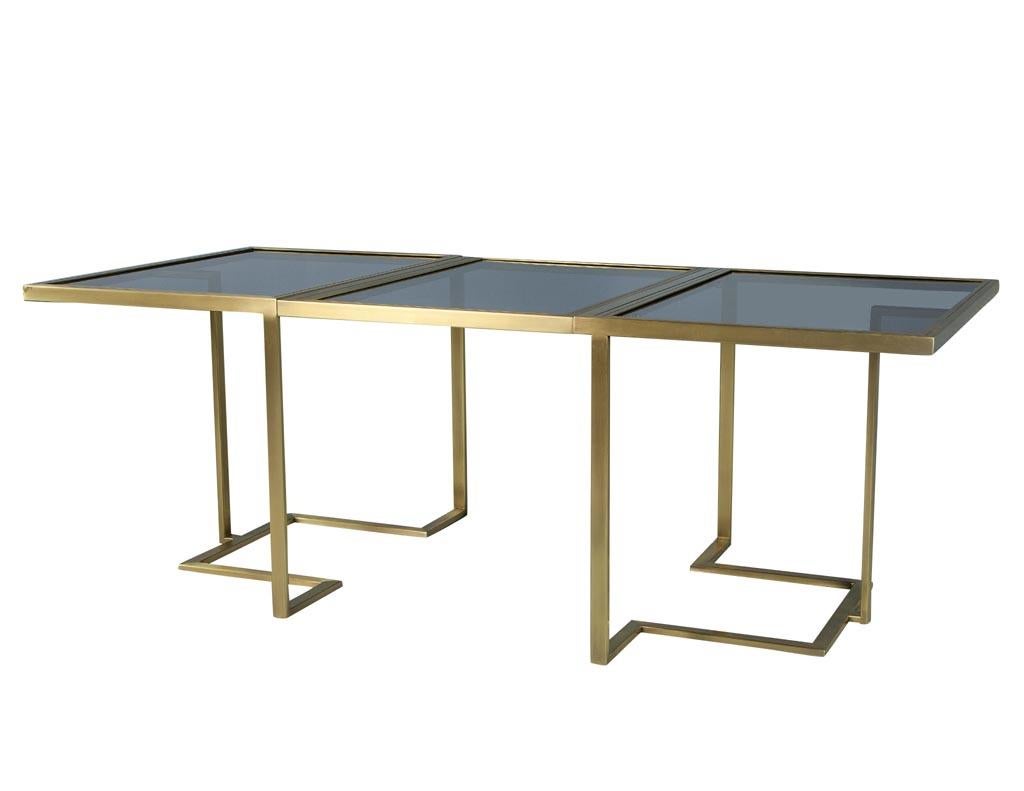 Custom modern brass dining table with glass top fully expandable by Carrocel. Made with brass and a smoked glass modern sleek design, this table closes to 55 ¼” and opens up to 83”. This table has that modern touch that can complement any interior