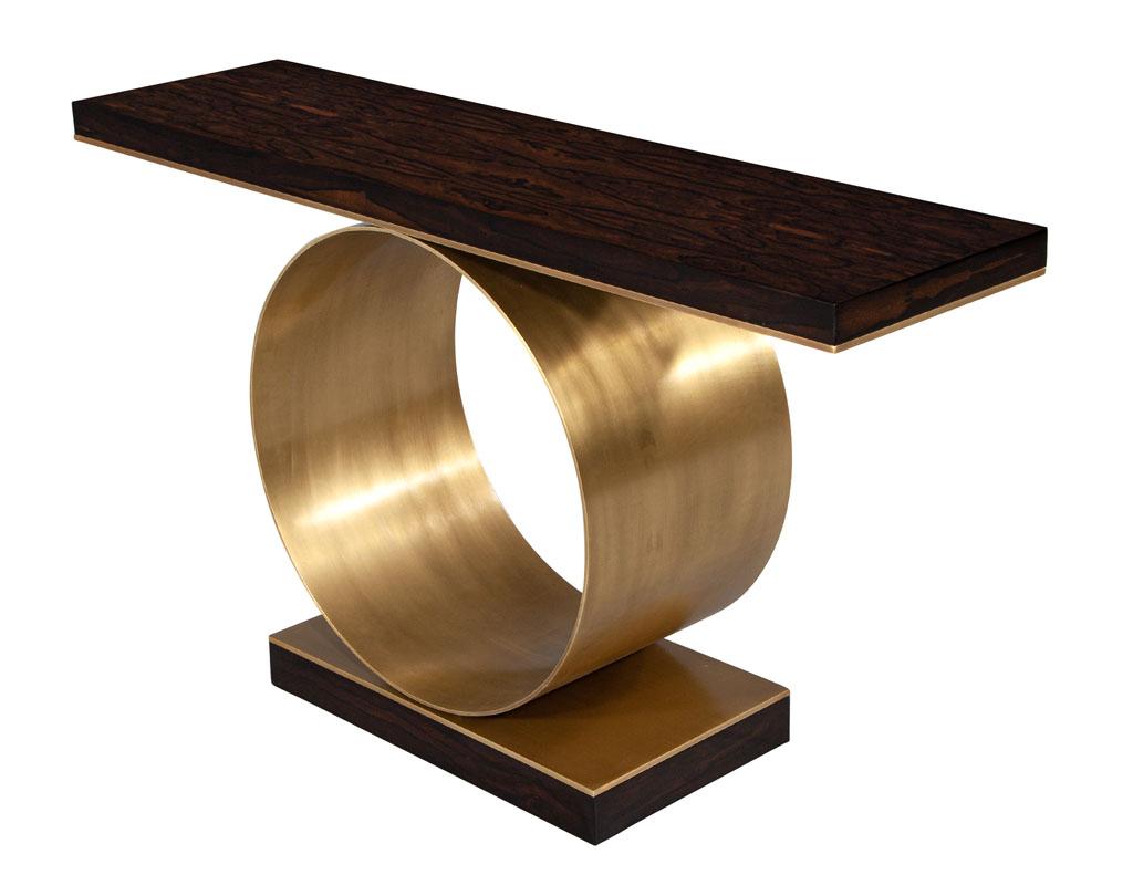 Custom Modern Console Table with Round Brass Pedestal. This custom-made, modern console table is crafted from ziricote wood with a unique wood grain pattern that will be sure to set it apart from the rest. The round brushed brass pedestal adds to