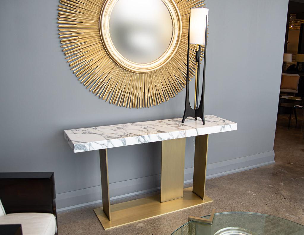 This custom made modern marble top console table is a work of art created by the Carrocel Artisans. Crafted by hand, the table is made of a rich Italian marble top with detailed veining in white and grey tones. The top rests on a custom brass plated