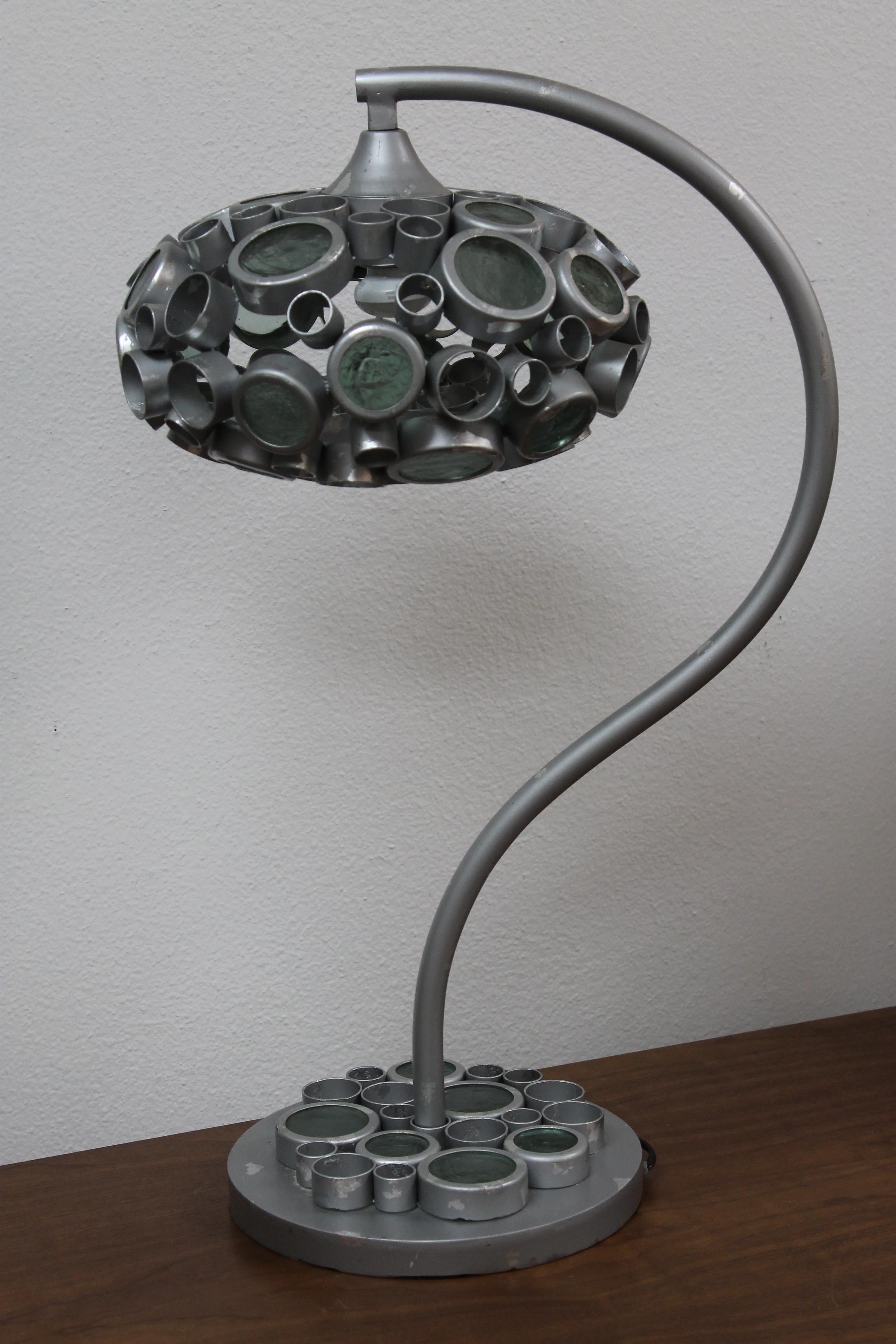 A hand crafted steel lamp with welded steel rings forming a mushroom shaped shade with textured clear pale green-grey glass. The glass seems to be about 1/4