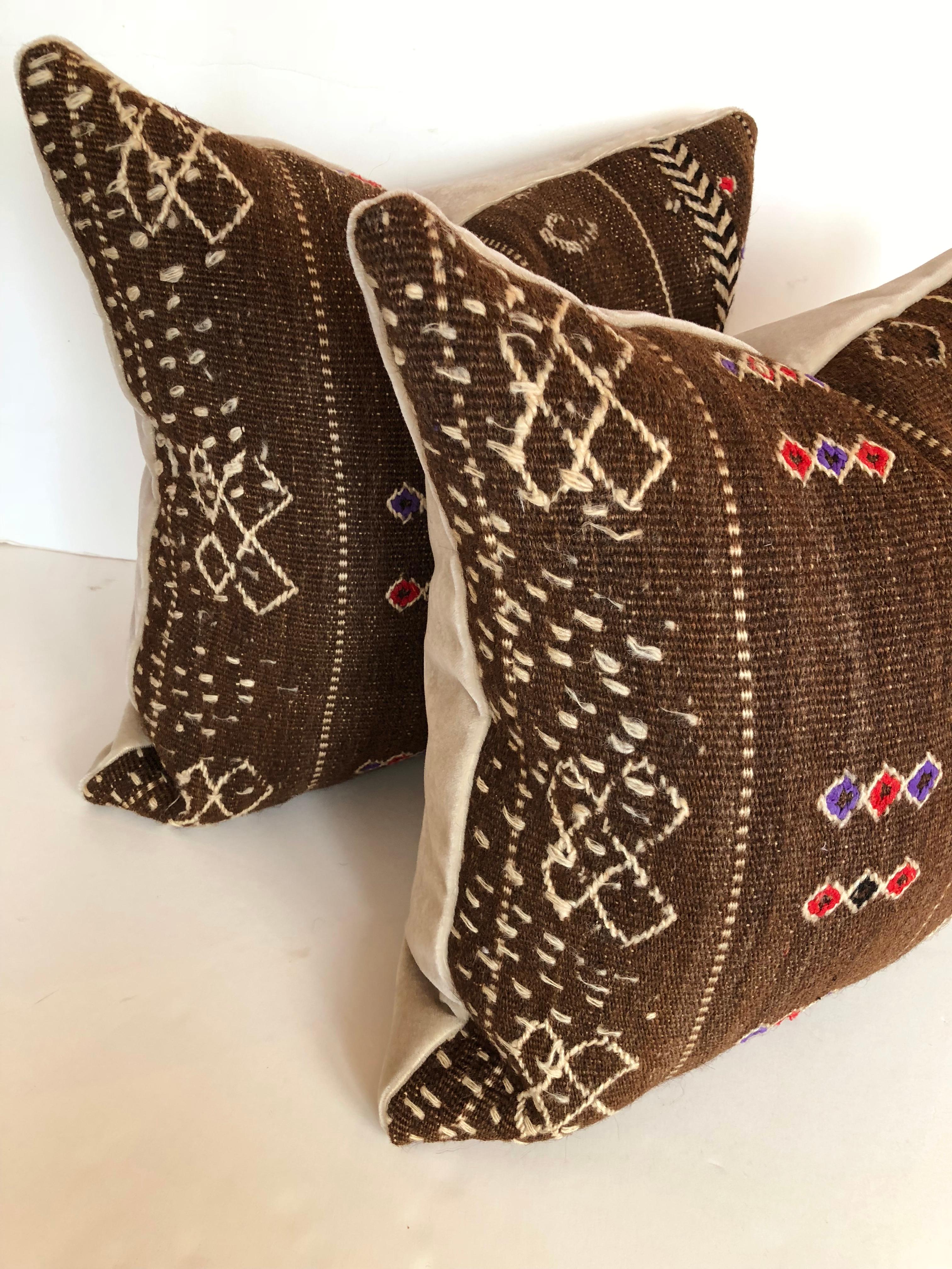 Custom pillows cut from a vintage hand loomed wool Moroccan Berber rug. Wool has decorative embroidered tribal designs. Pillows are backed in a cream mohair, filled with an insert of 50/50 down and feathers and hand sewn closed. Pillows sold