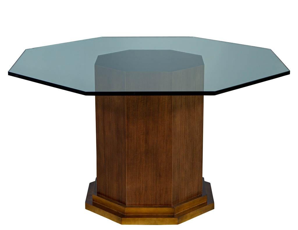This Carrocel custom pedestal features a hexagon design. Constructed of solid walnut, finished in a walnut stain and accented with an aged, gold leaf base step detail. Sitting atop this sleek pedestal is a polished edge, octagon glass table.